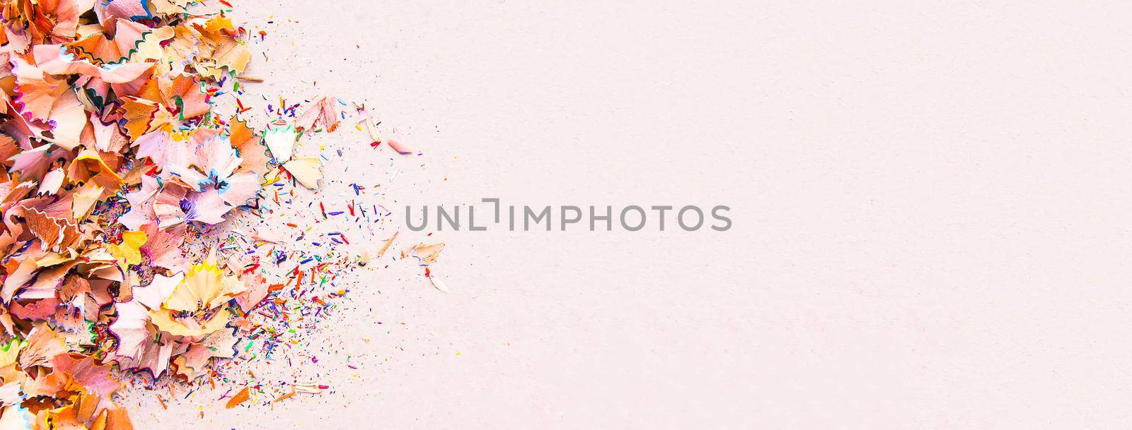 Wooden pencil shavings and colorful crumbs of graphite from sharpener on soft pink paper background. Top view. Design elements for poster, banner, cards.
