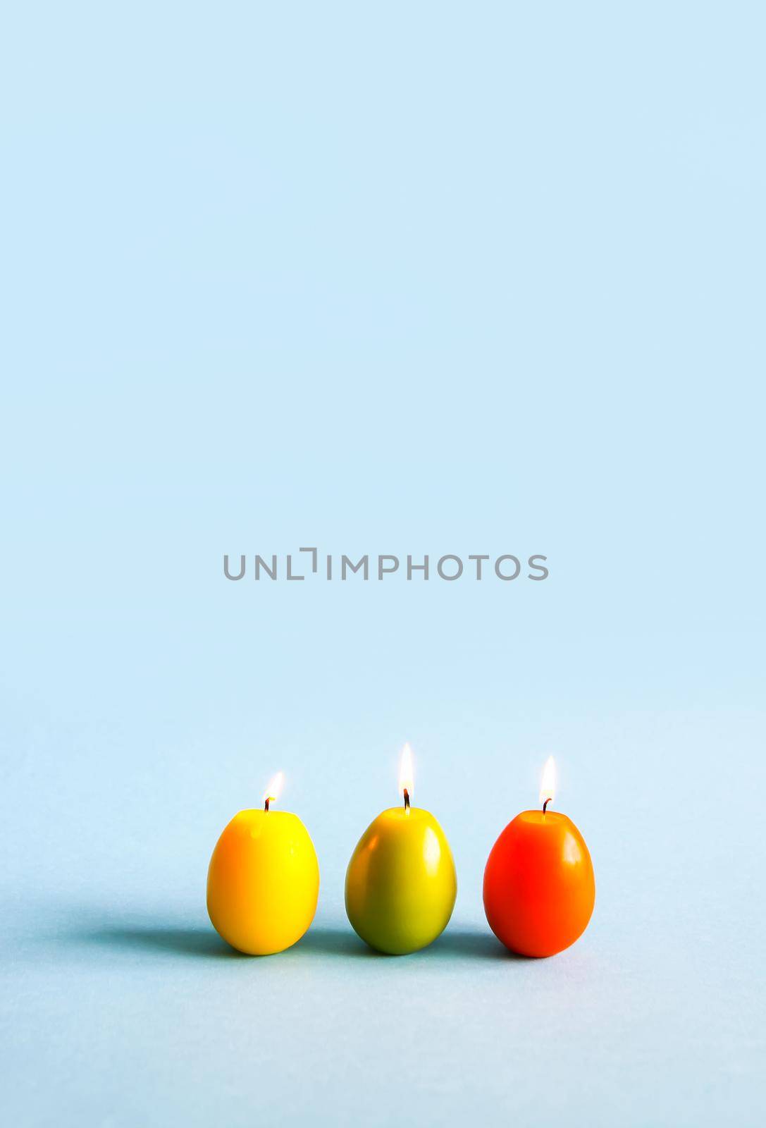Traditional Easter decor. Bright burning paraffin candles in the shape of colorful eggs on blue background.