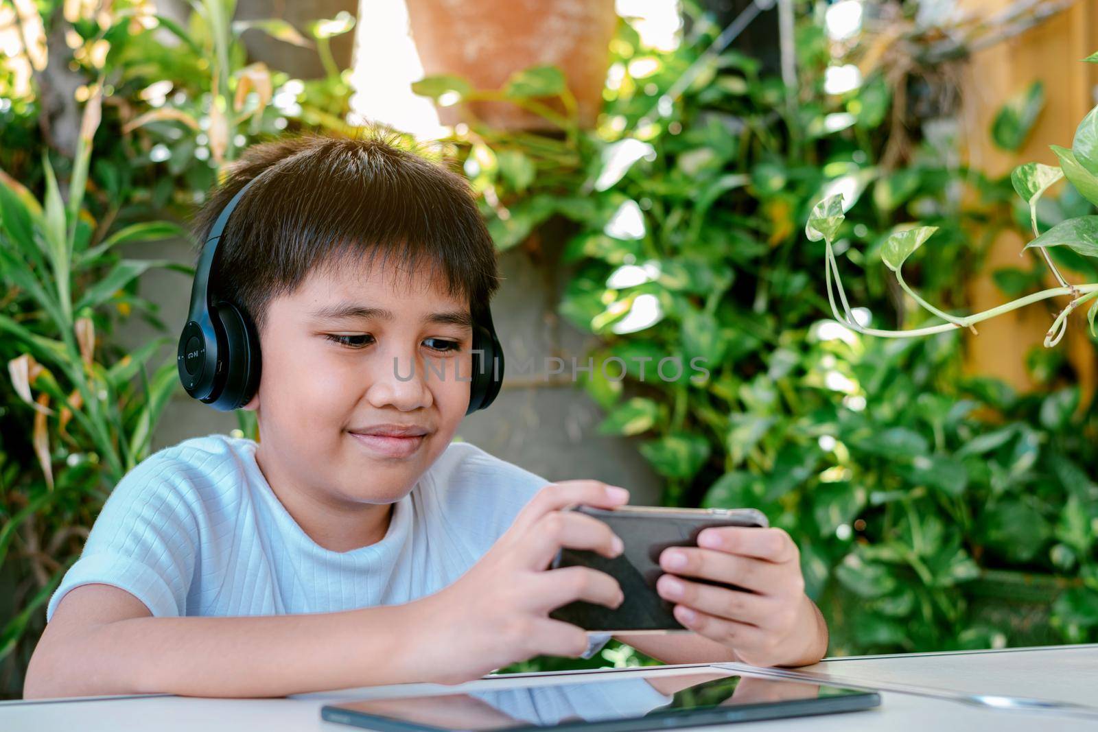 Asian boy wearing headphones and white shirt smiling and play games on his smart phone.