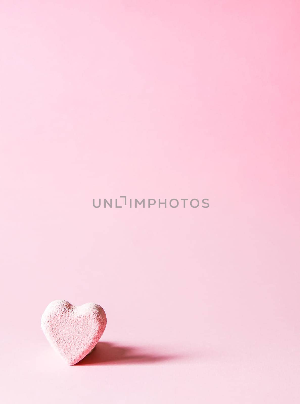 Pink small bath bomb in the shape of heart on soft pastel background