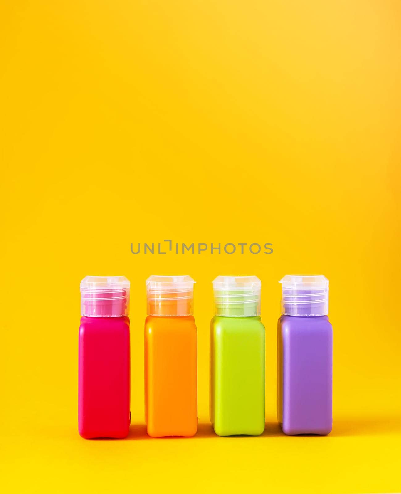 Colorful plastic bottles for skincare products on bright yellow background