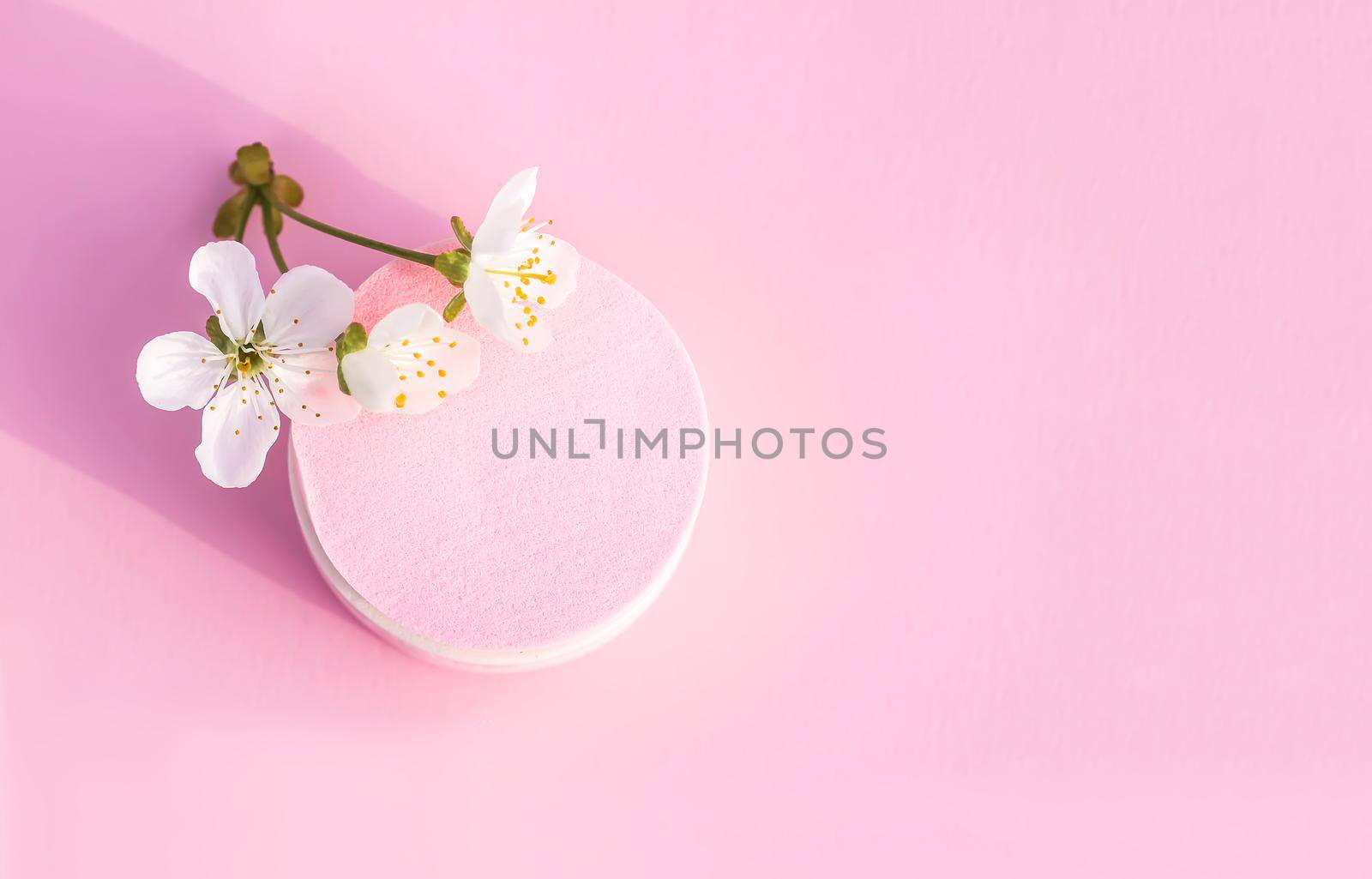 Cosmetic sponges and cherry tree branch with spring flowers on pink pastel paper background.