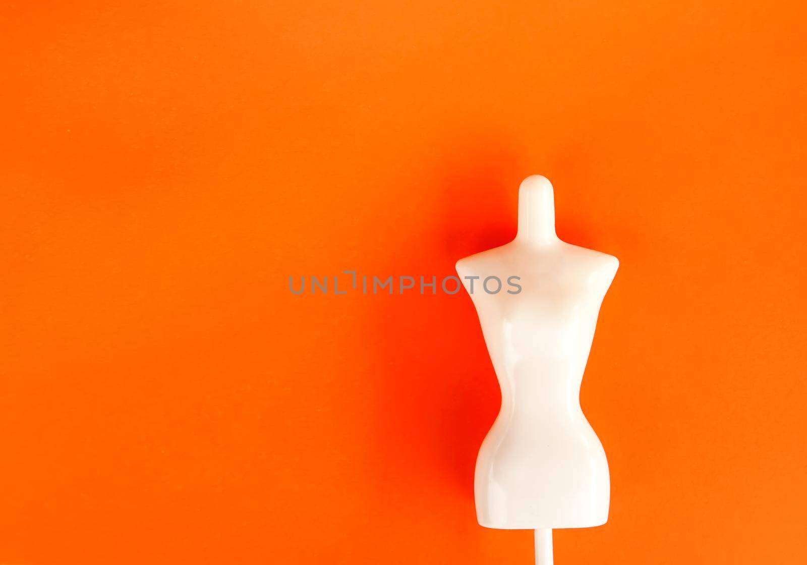 White plastic female mannequin figure on bright orange background.