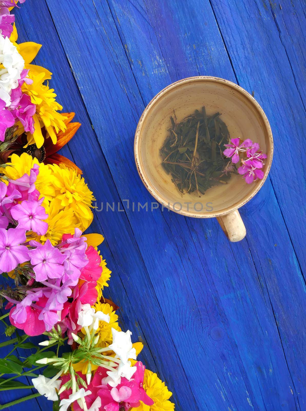 Natural herbal tea with purple fresh flowers and leaves of medical fireweed plant n ceramic cup on blue wooden boards outdoors.
