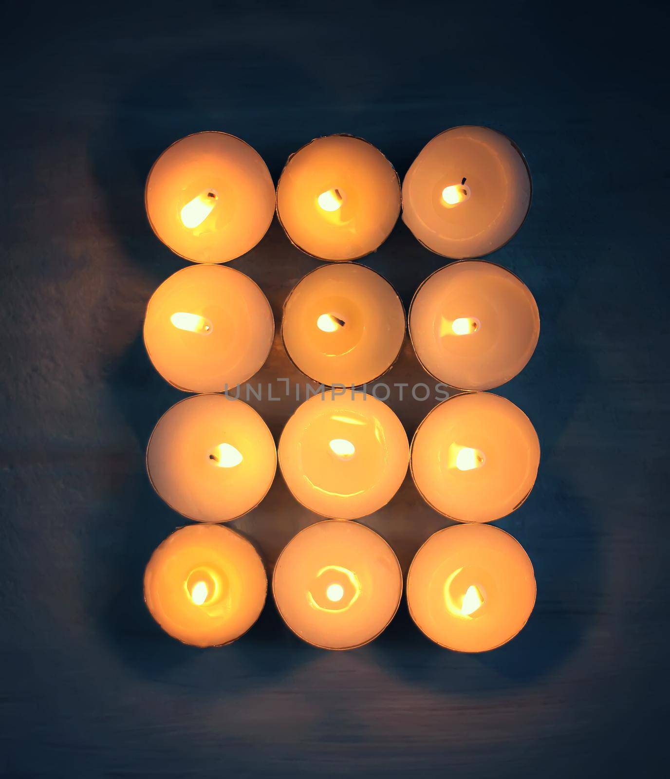 12 burning candles on dark background.