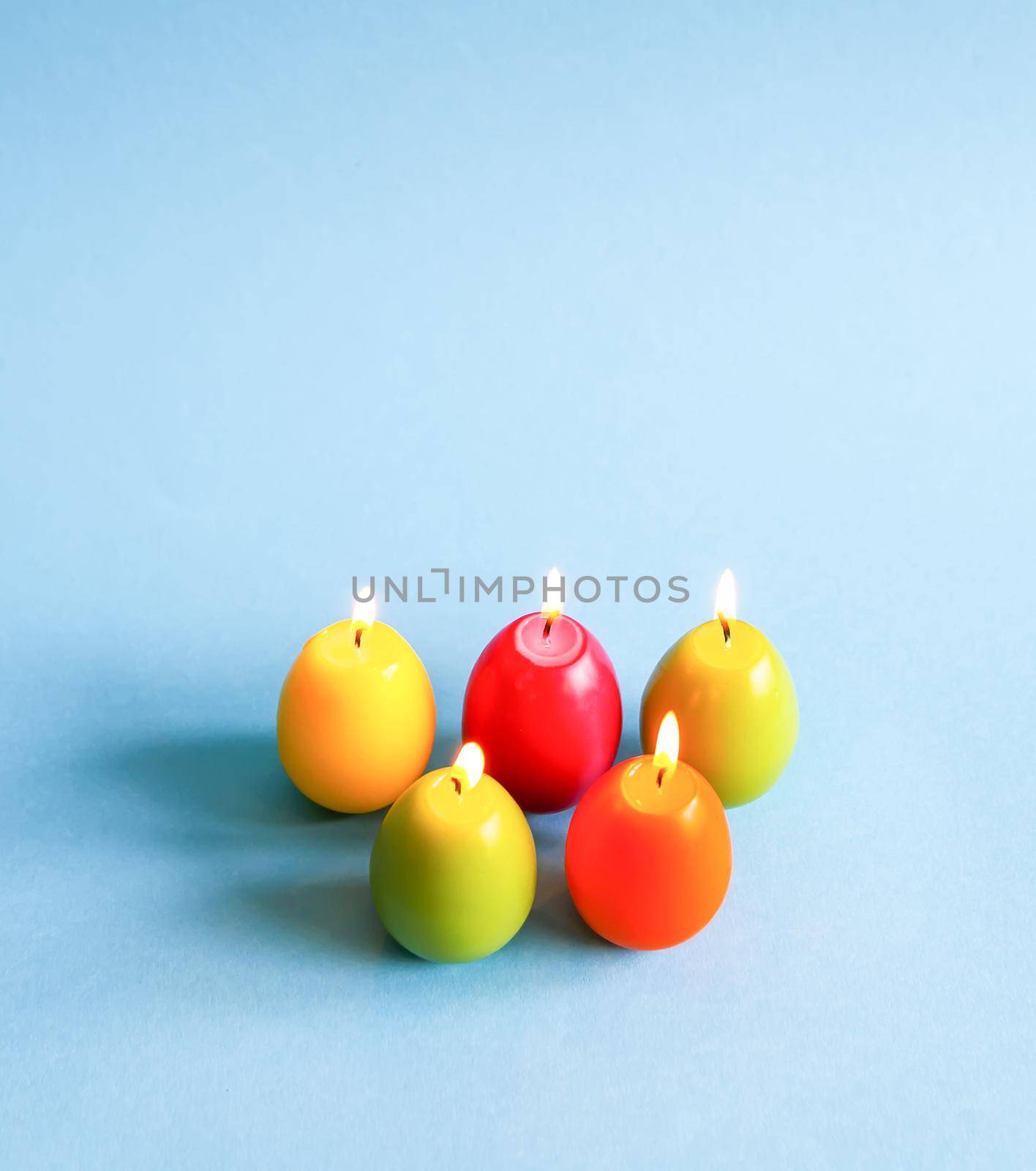 Traditional Easter decor. Bright burning paraffin candles in the shape of colorful eggs on blue background.