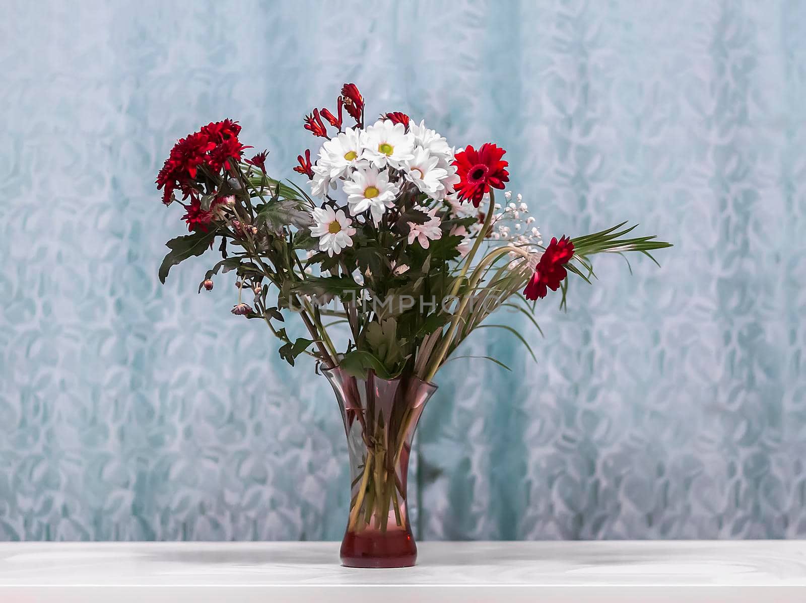 Bouquet of flowers in glass vase on white table in room interior