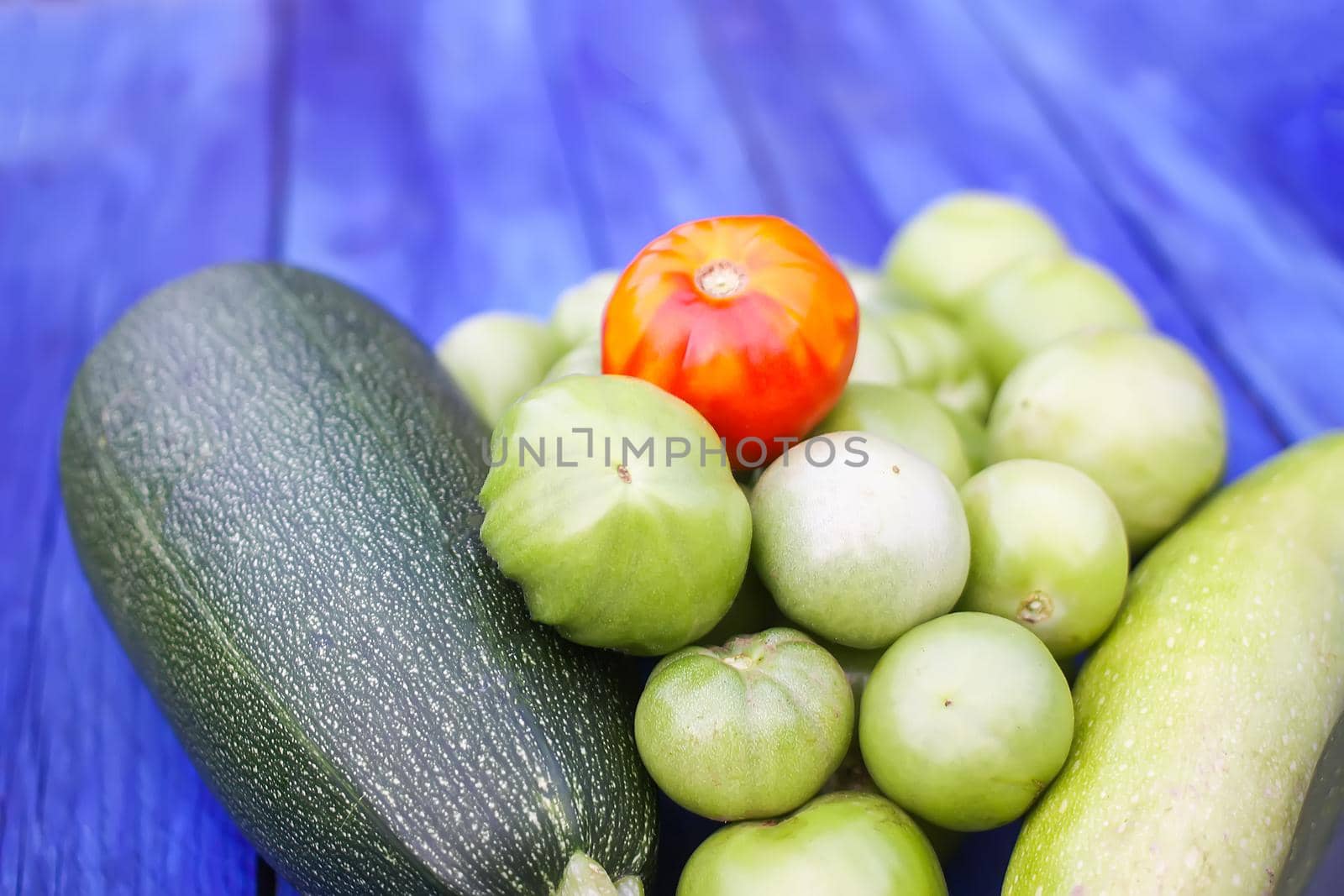 Zucchini and unripe tomatoes. Fresh raw organic vegetables on wooden boards outdoors.