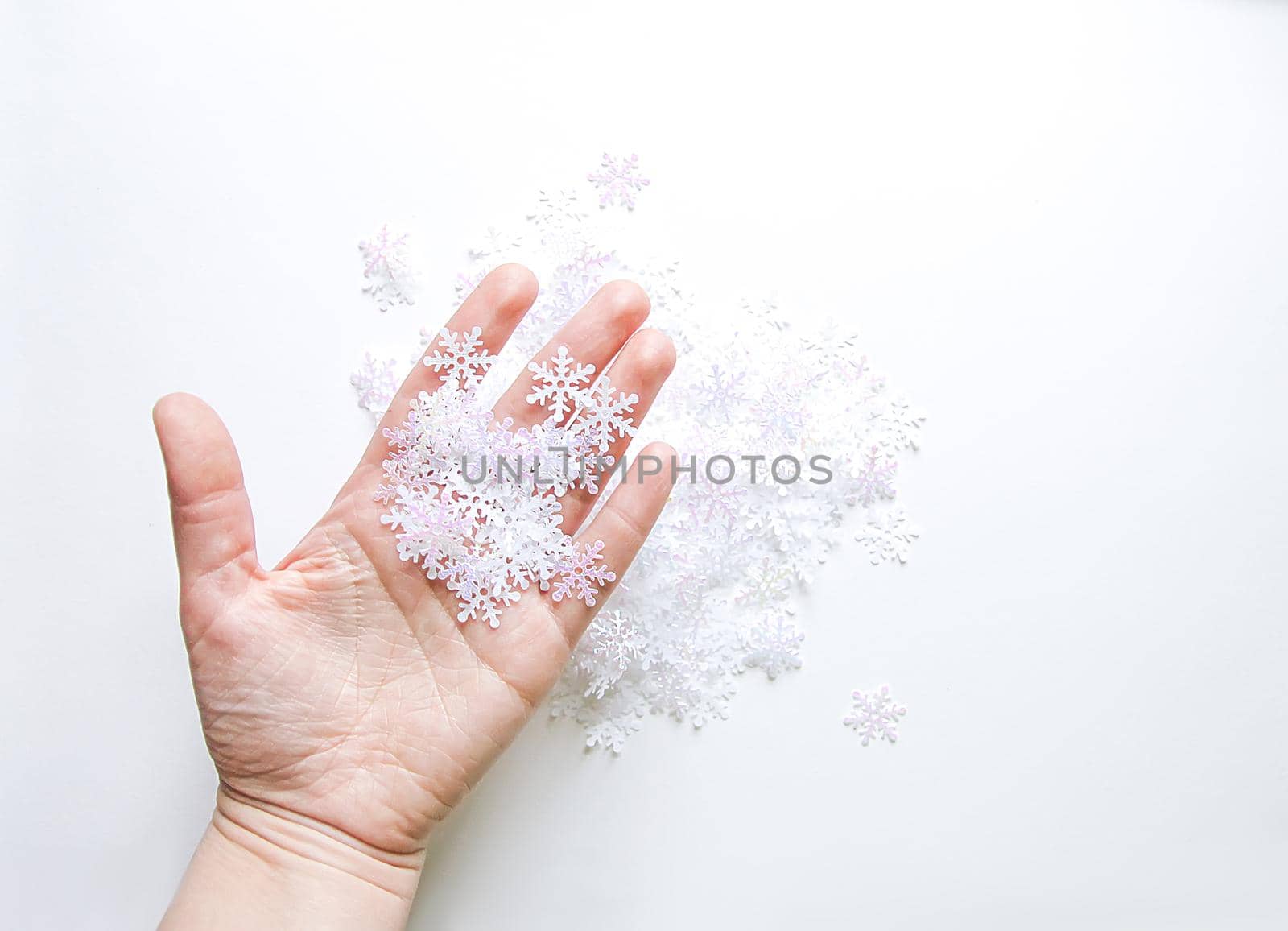 White artificial snowflakes in a woman's hand on soft light background. Winter background. Decorative template for cards, banner, poster.