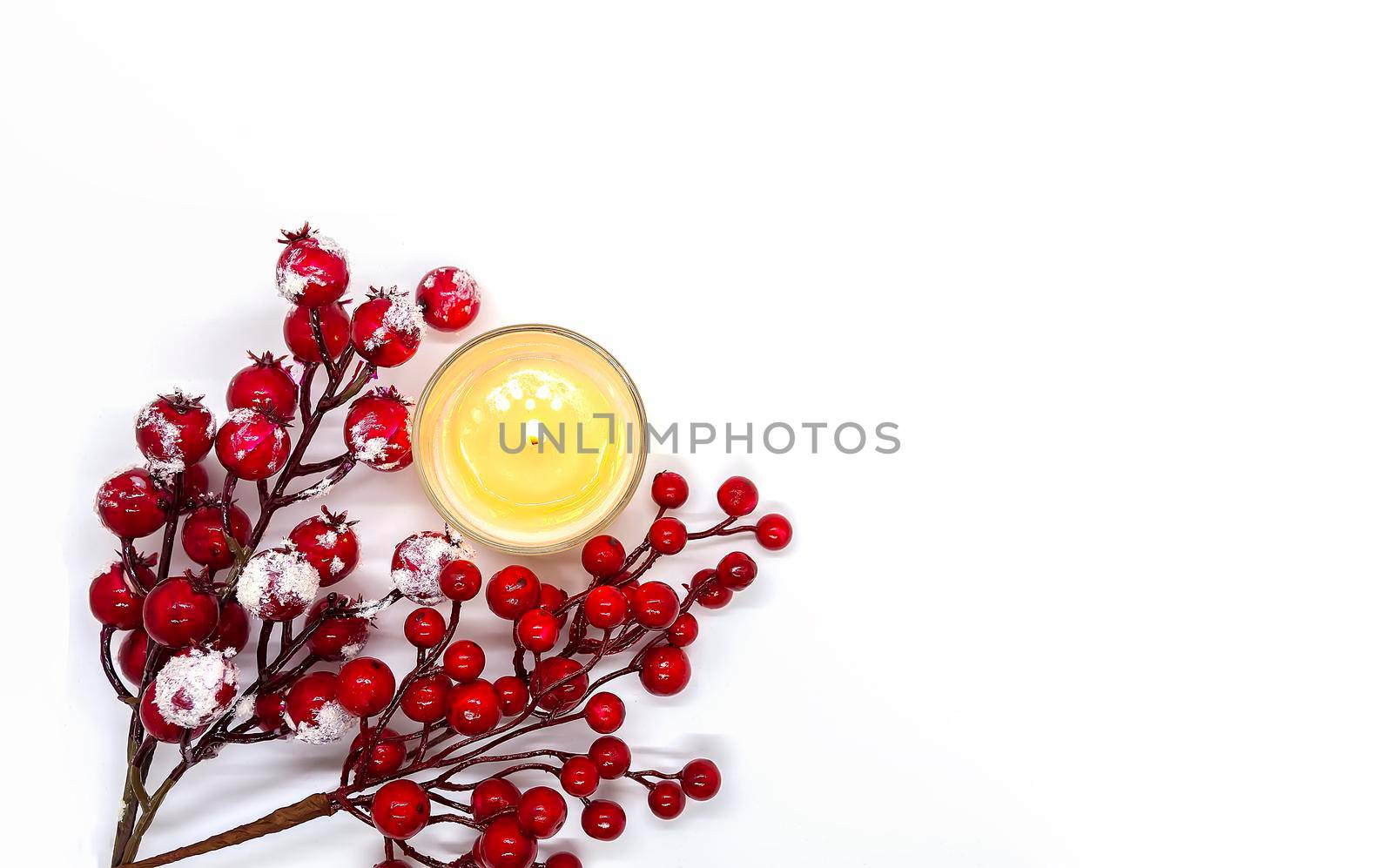 Festive Christmas or New Year composition with red holly berries in snow and burning wax candle on white background
