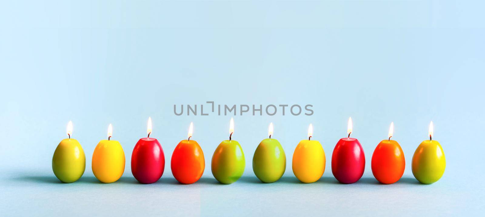 Traditional Easter decor. Bright burning paraffin candles in the shape of colorful eggs on blue background.