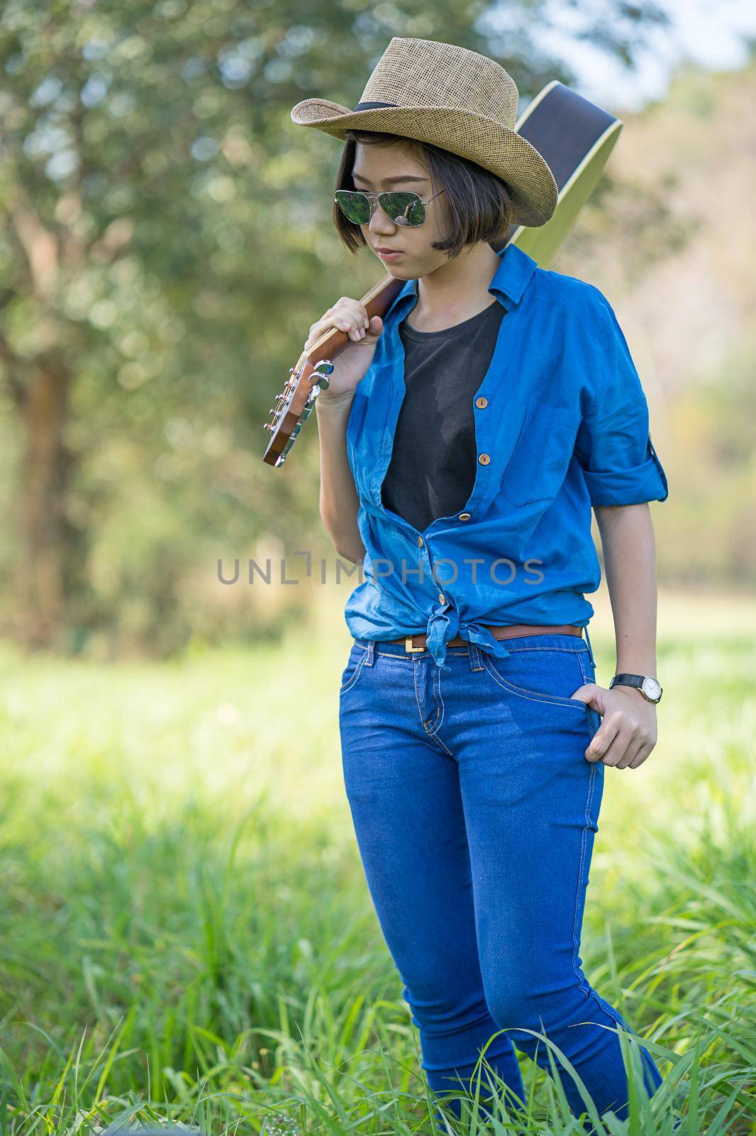 Woman wear hat and carry her guitar in grass field  by stoonn