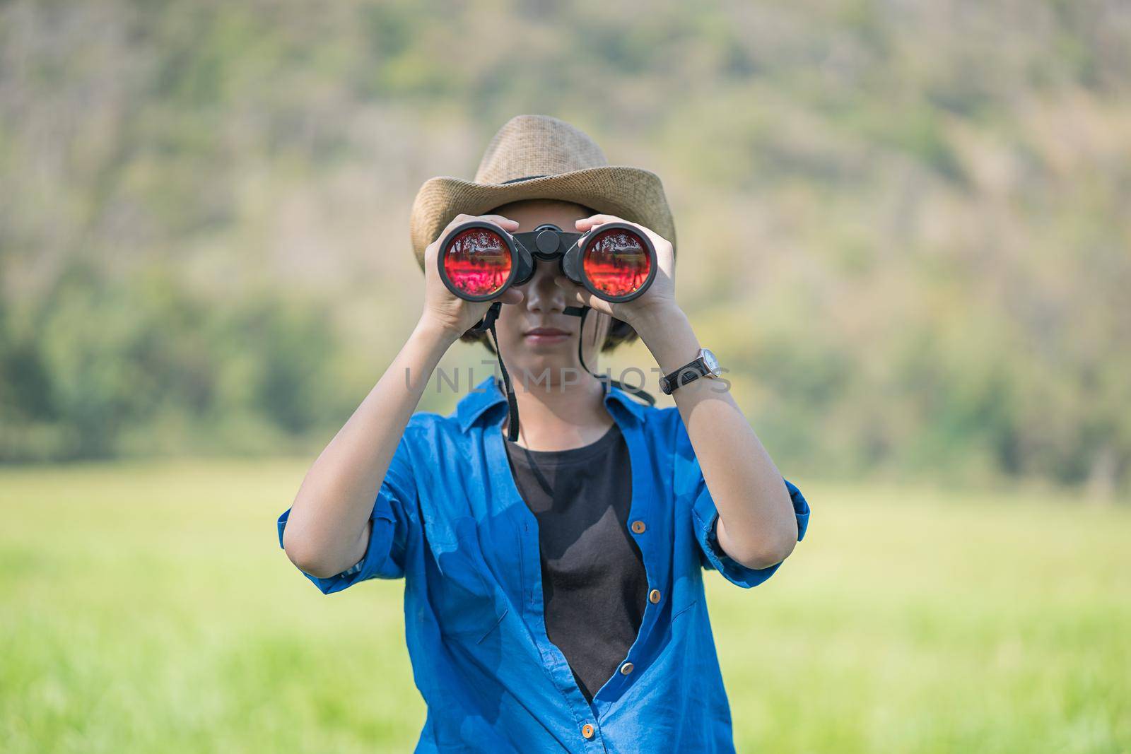 Young asian woman short hair wear hat and hold binocular in grass field countryside Thailand