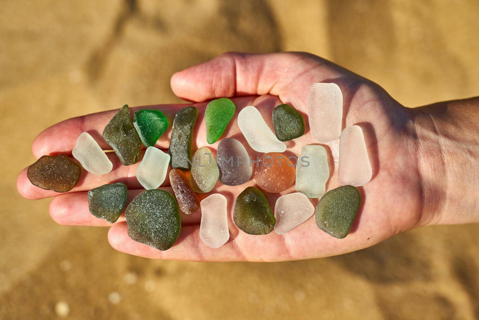 A persons open palm holds various colours of sea glass