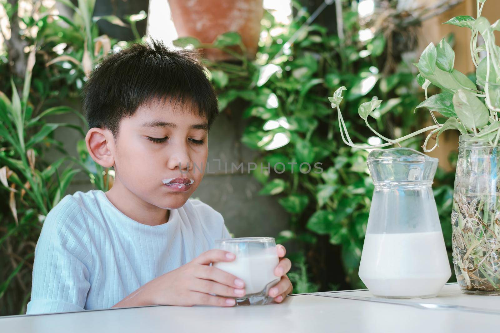 Asian boy in a white T-shirt is drinking a glass of milk. by wattanaphob