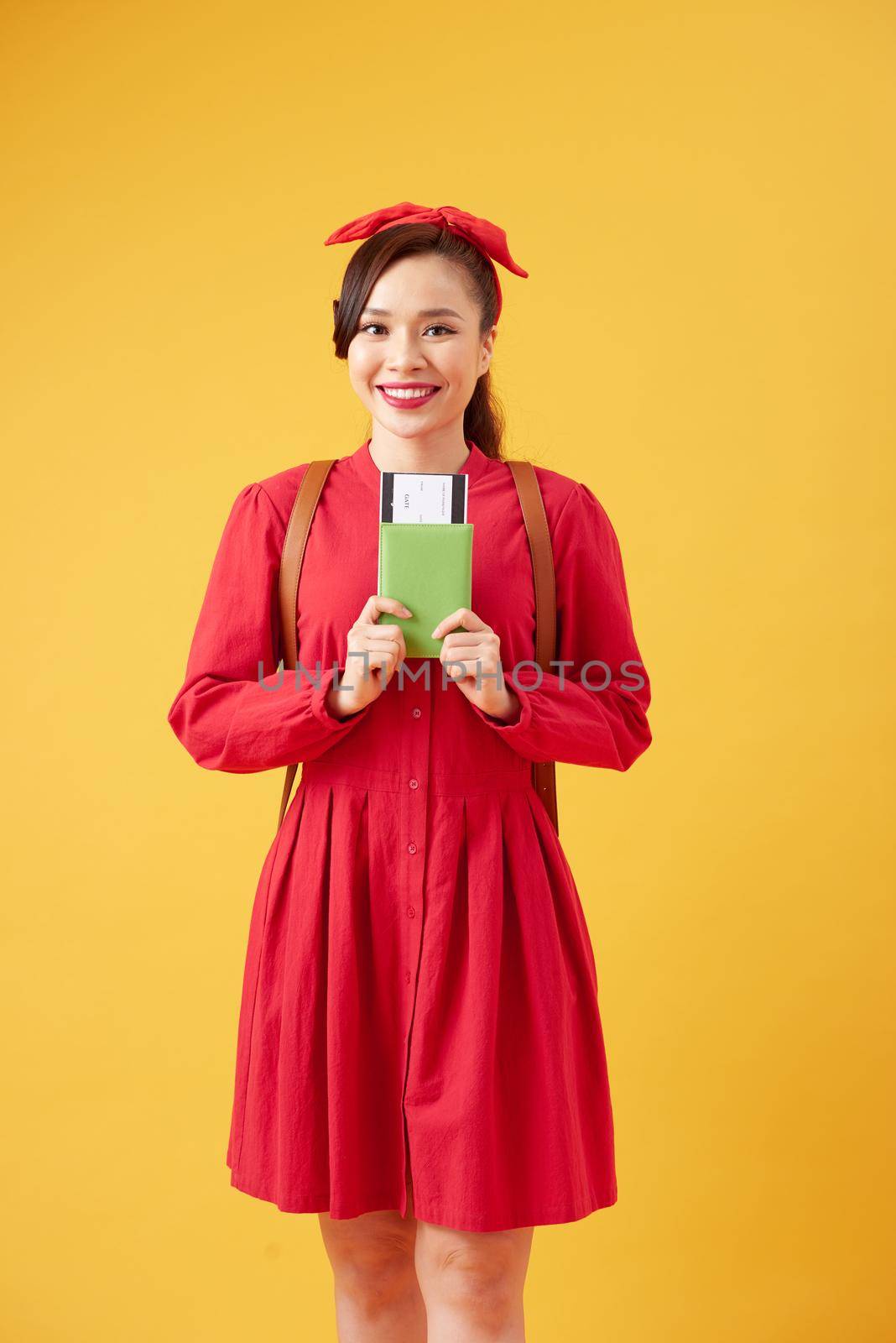 Travel and Lifestyle concept: Full length studio portrait of pretty young student woman holding passport with tickets. Isolated on bright yellow background. by makidotvn