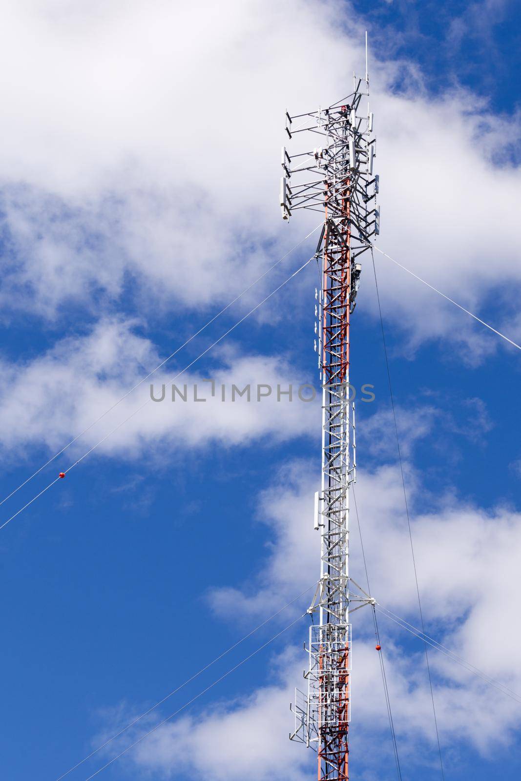 Metal lattice truss tower with telecommunication antennas against clouds and blue sky