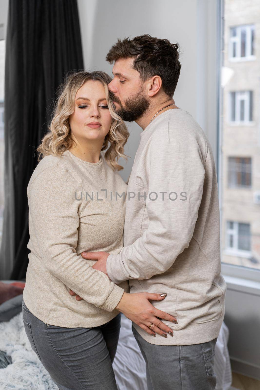 Happy family concept. Husband hug belly pregnant wife standing indoor living room near sofa by andreonegin
