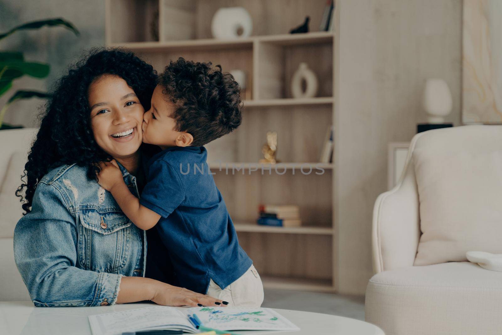 Portrait of afro american cute boy in blue polo tshirt hugging mother and kissing her in cheek by vkstock