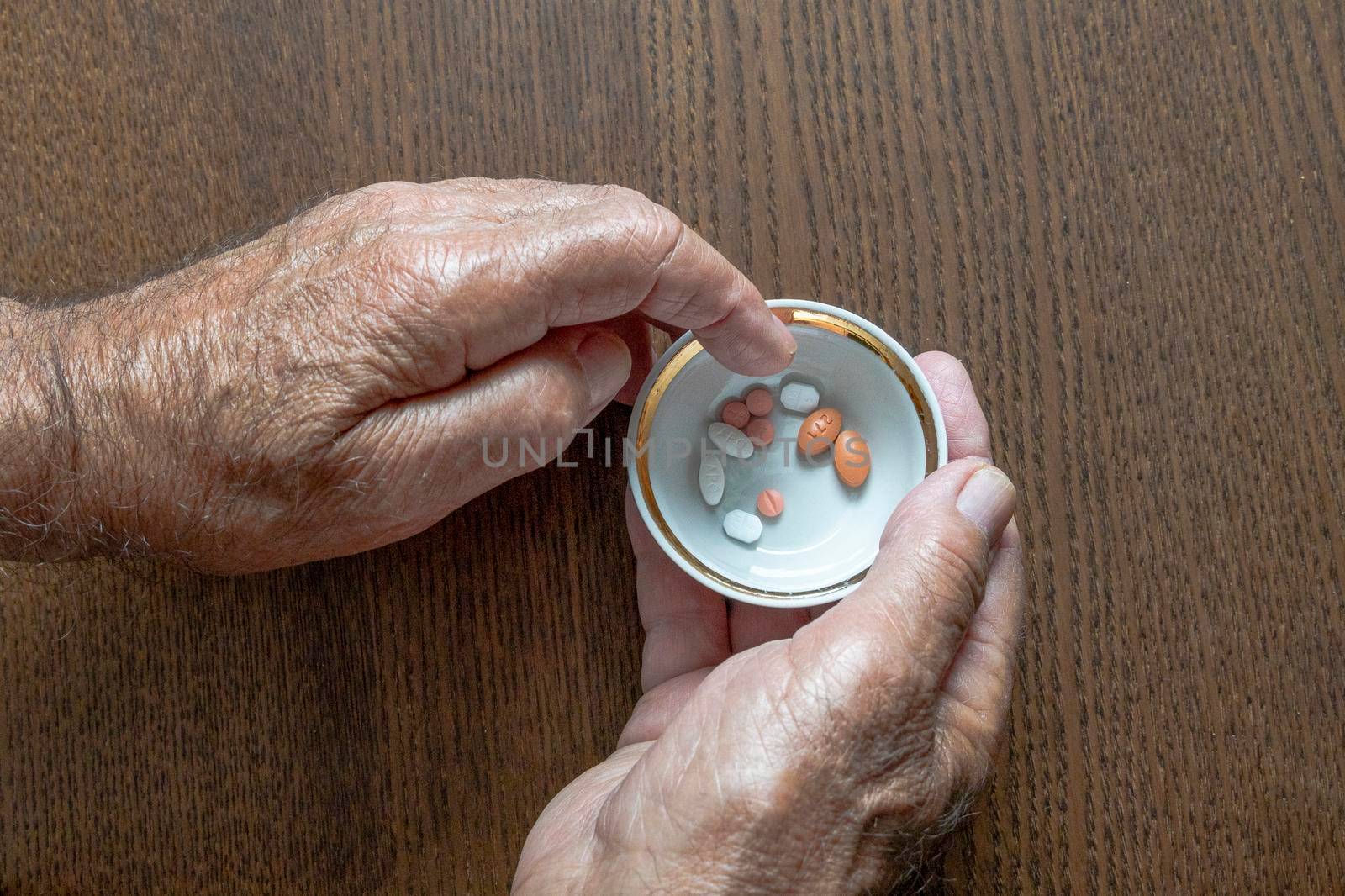 An elderly man holding a cup of pills in his hands selects the desired pill from it