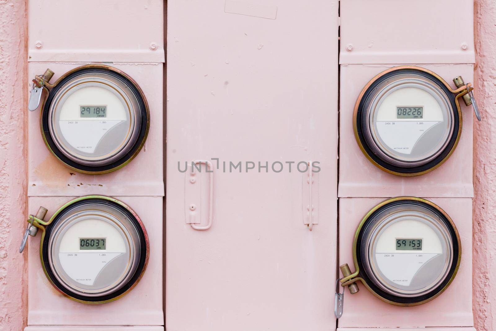 Array of four modern smart grid residential digital power supply watthour meters on grungy pink exterior wall