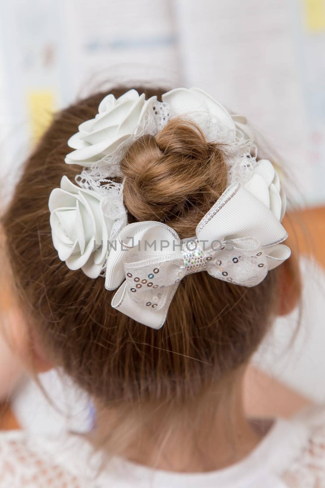 Close-up of a girl's hairstyle with a bun of hair tied with a white bow. Hair styling is done with a bow with an elastic band. Only the back of the head with a haircut