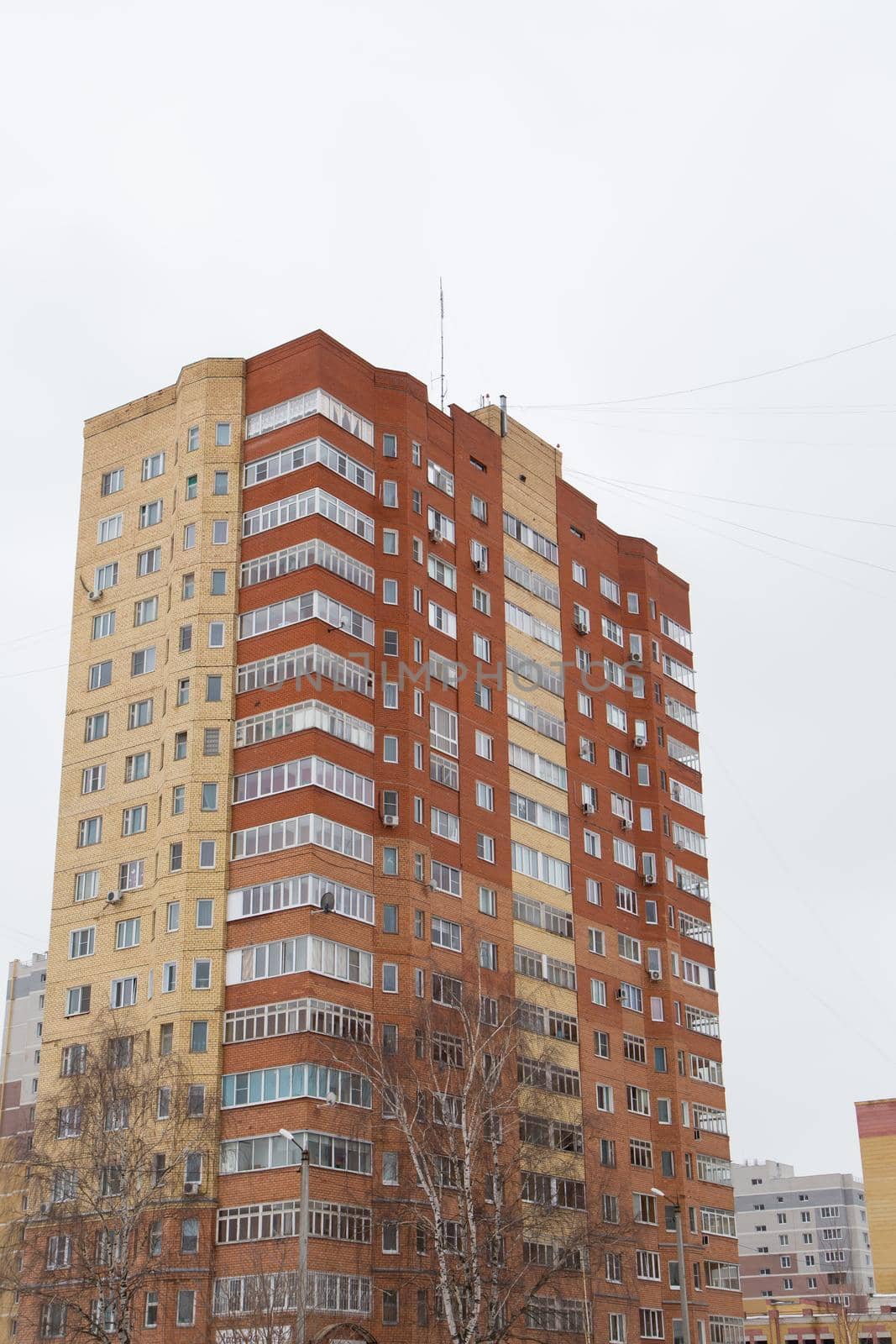 Residential high-rise building made of red and yellow bricks with balconies. Against the background of the gray sky. Modern new buildings, building facades. Real estate and urban architecture concept.
