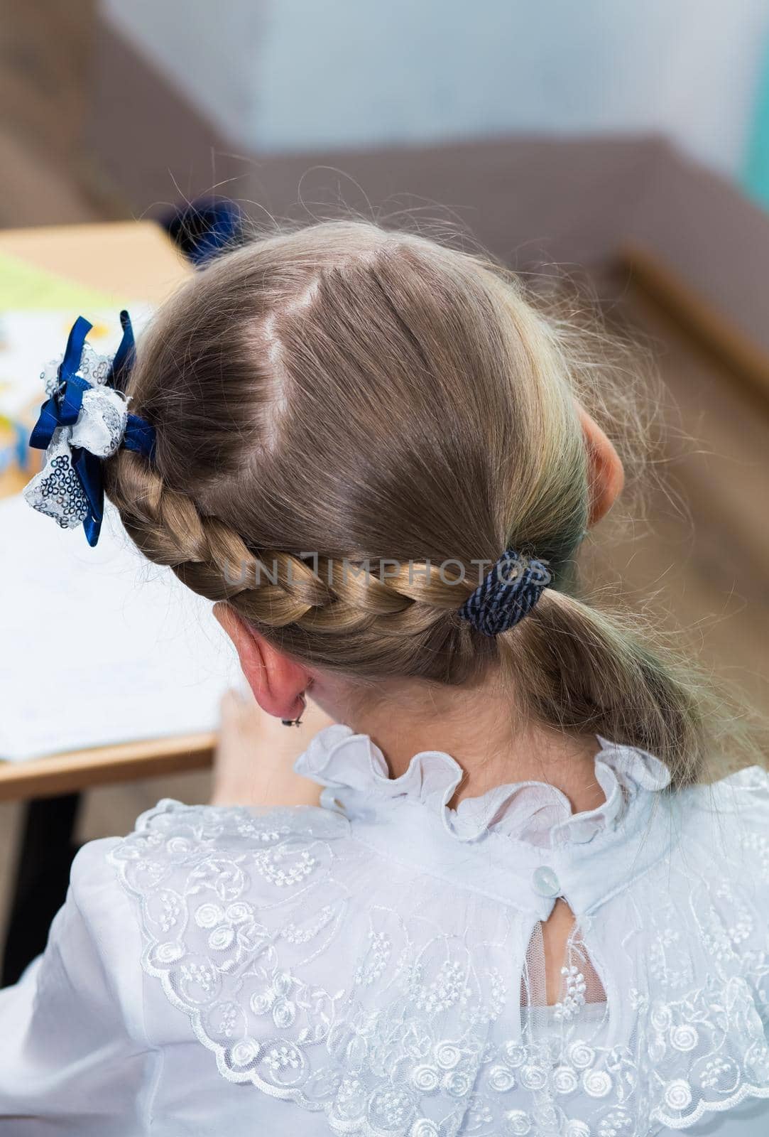 A girl's hairstyle with a braid around her head and a blue bow close-up. Hair styling is done with hairpins and an elastic band. Only the back of the head with a haircut.