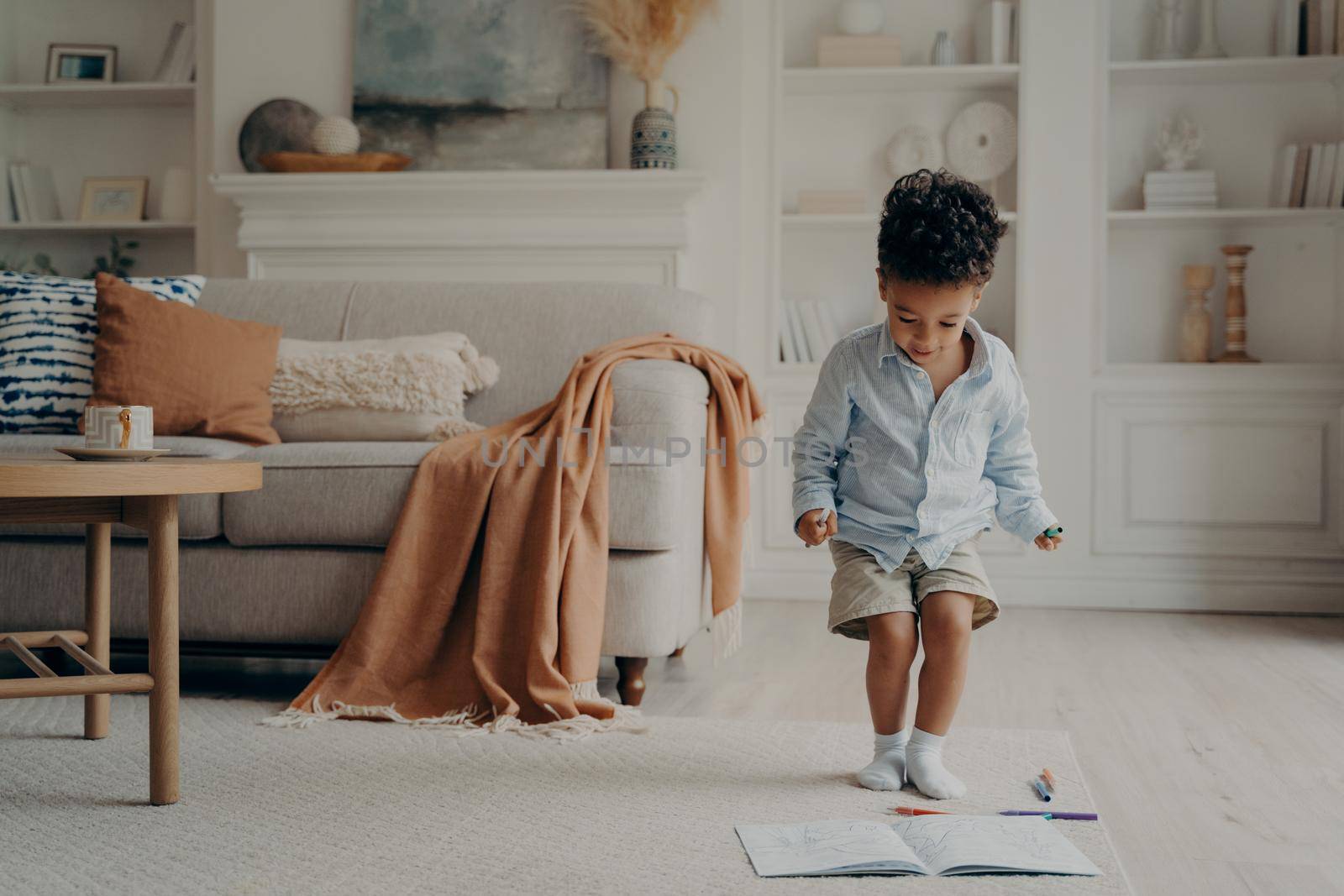 Happy mixed race little boy enjoying playing alone, drawing with pencils on warm carpeted floor, cute smiling african american kid having fun at home. Creative children activity indoor concept