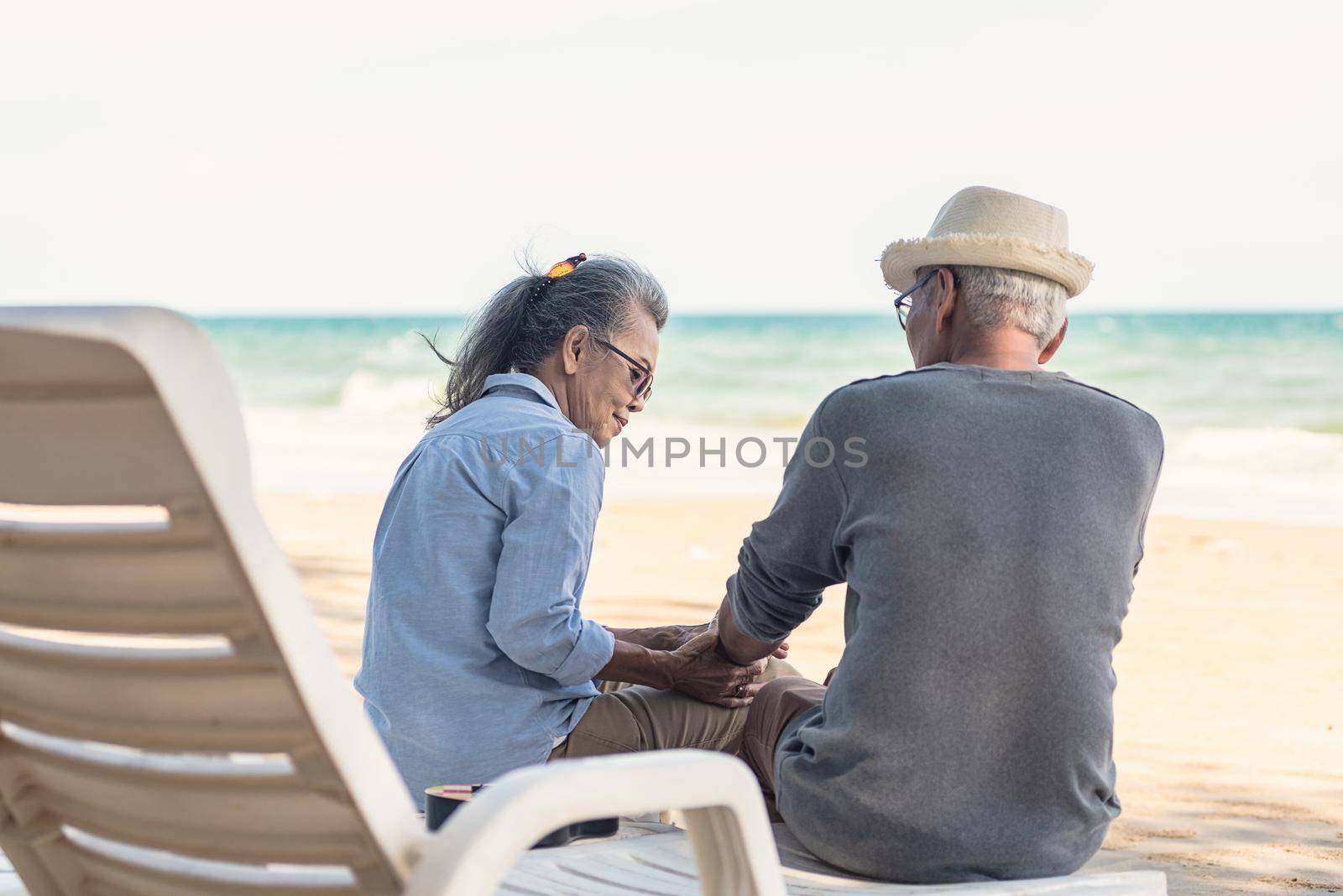 Happy Asian family, senior couple sitting on chairs with backs on beach travel vacation talking together by Sorapop