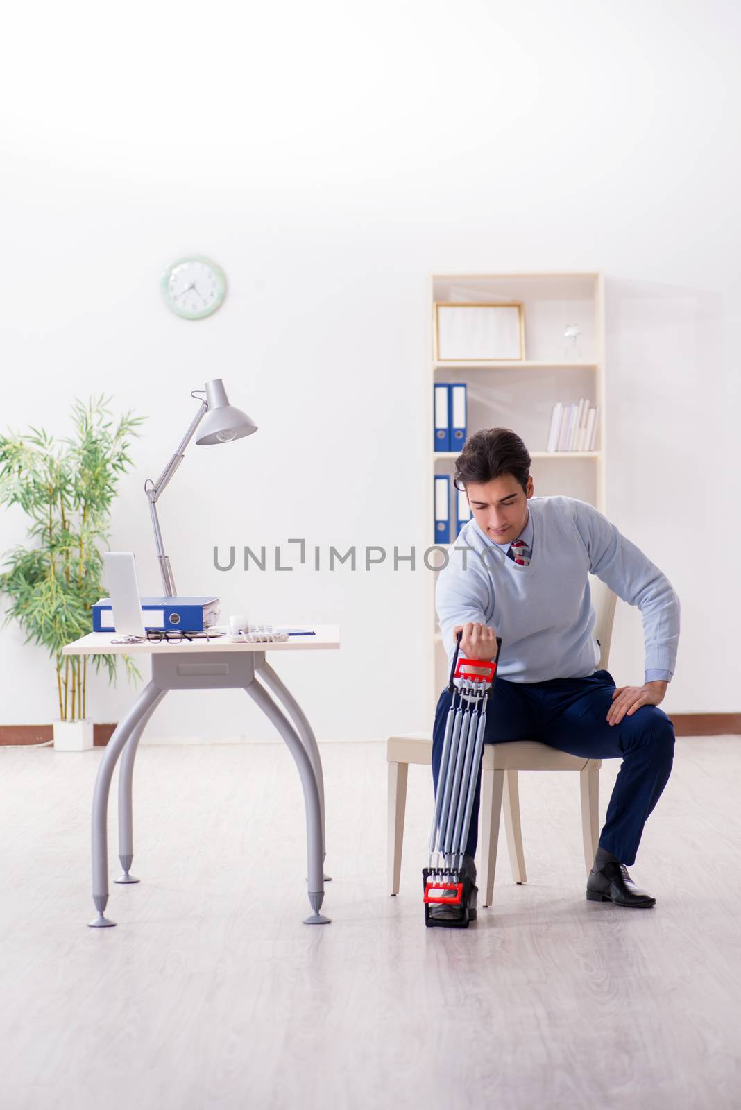 Man exercising with elastic band in office during lunch break by Elnur