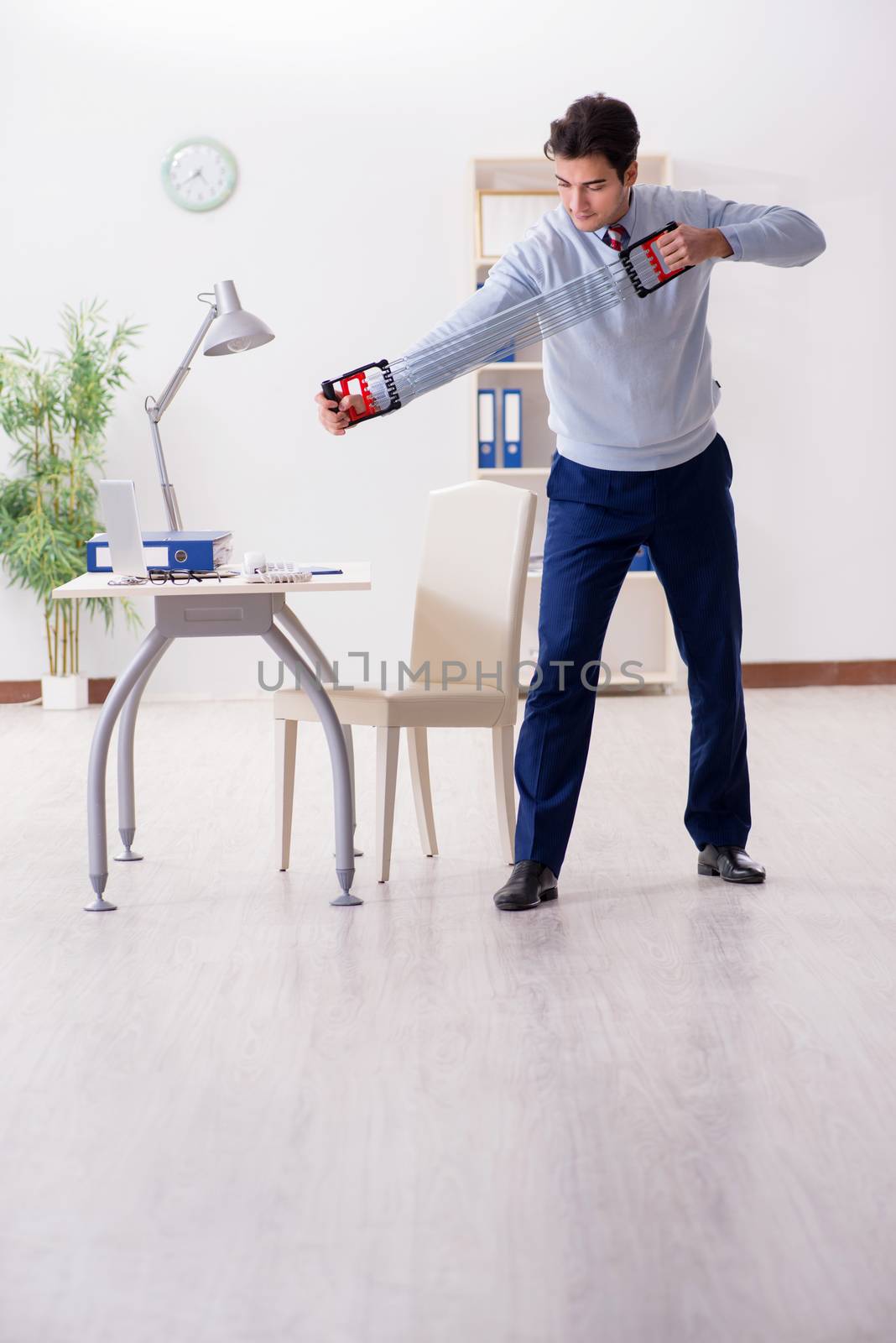 Man exercising with elastic band in office during lunch break by Elnur