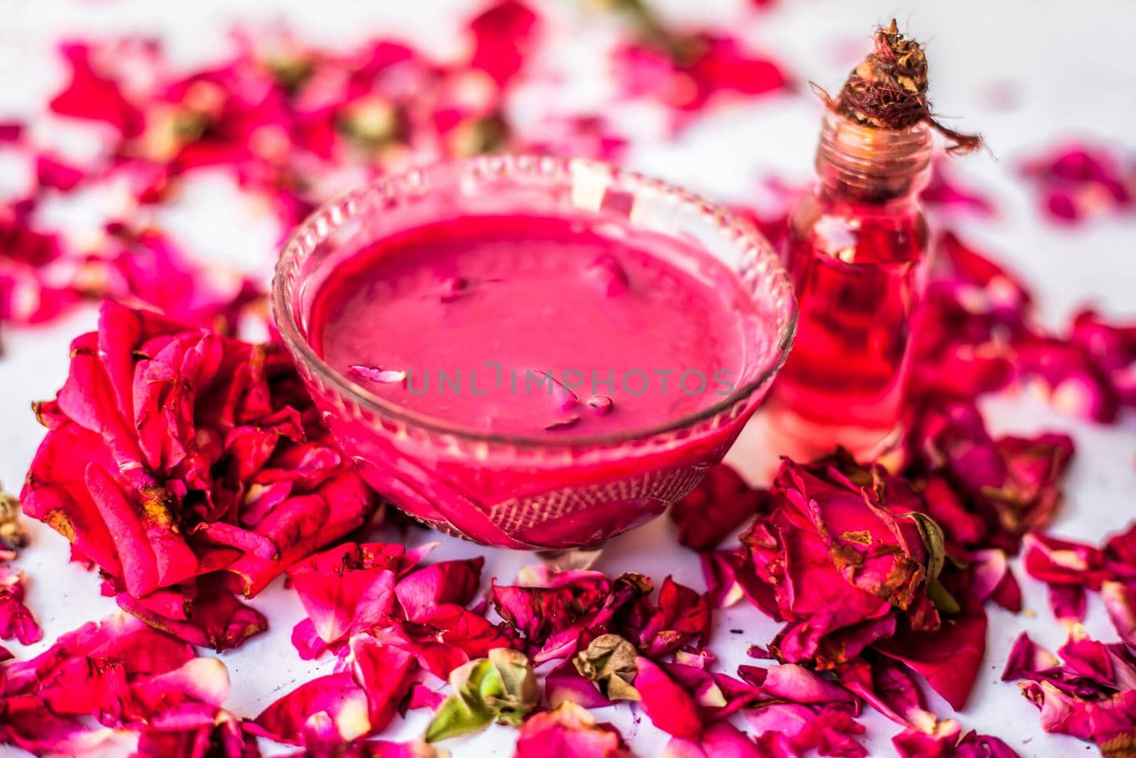 Rose Jam in a glass bowl with some essential oil or concentration of rose in a glass bottle along with some rose petals spread on the surface. by mirzamlk
