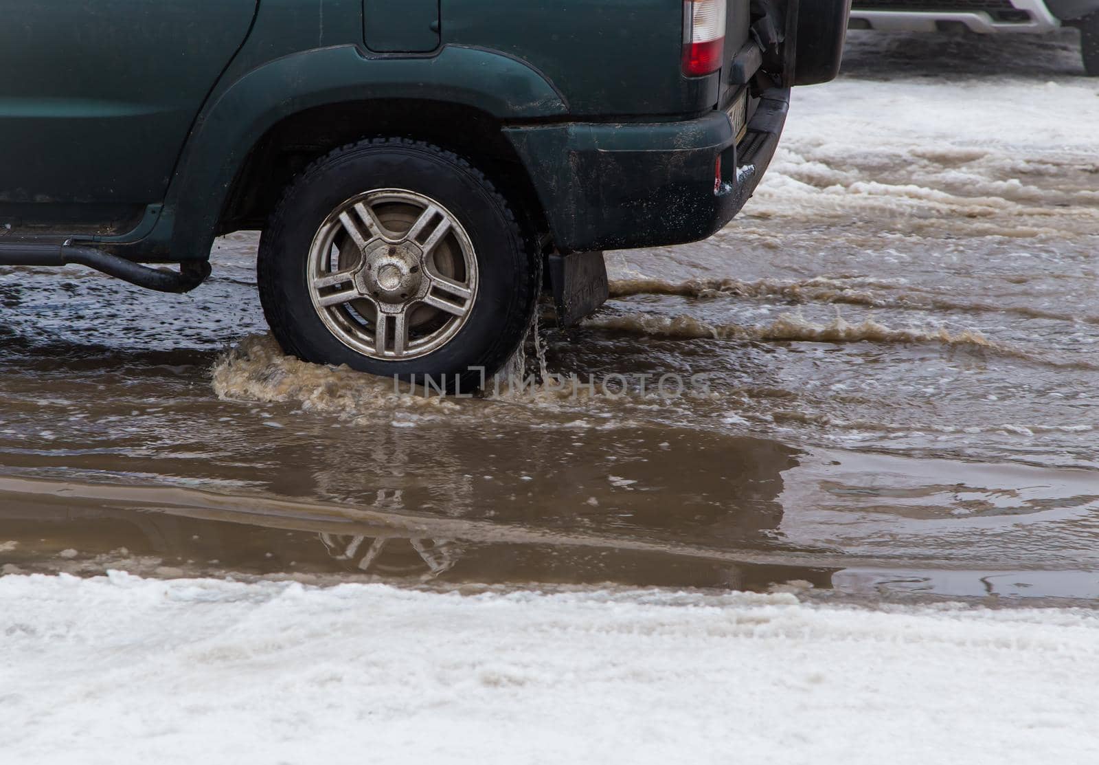 The wheel of a car driving through a deep puddle of melted snow. Abnormal weather concept. There is copy space. The New Year and Christmas celebrations are over. Remains of last year's snow.