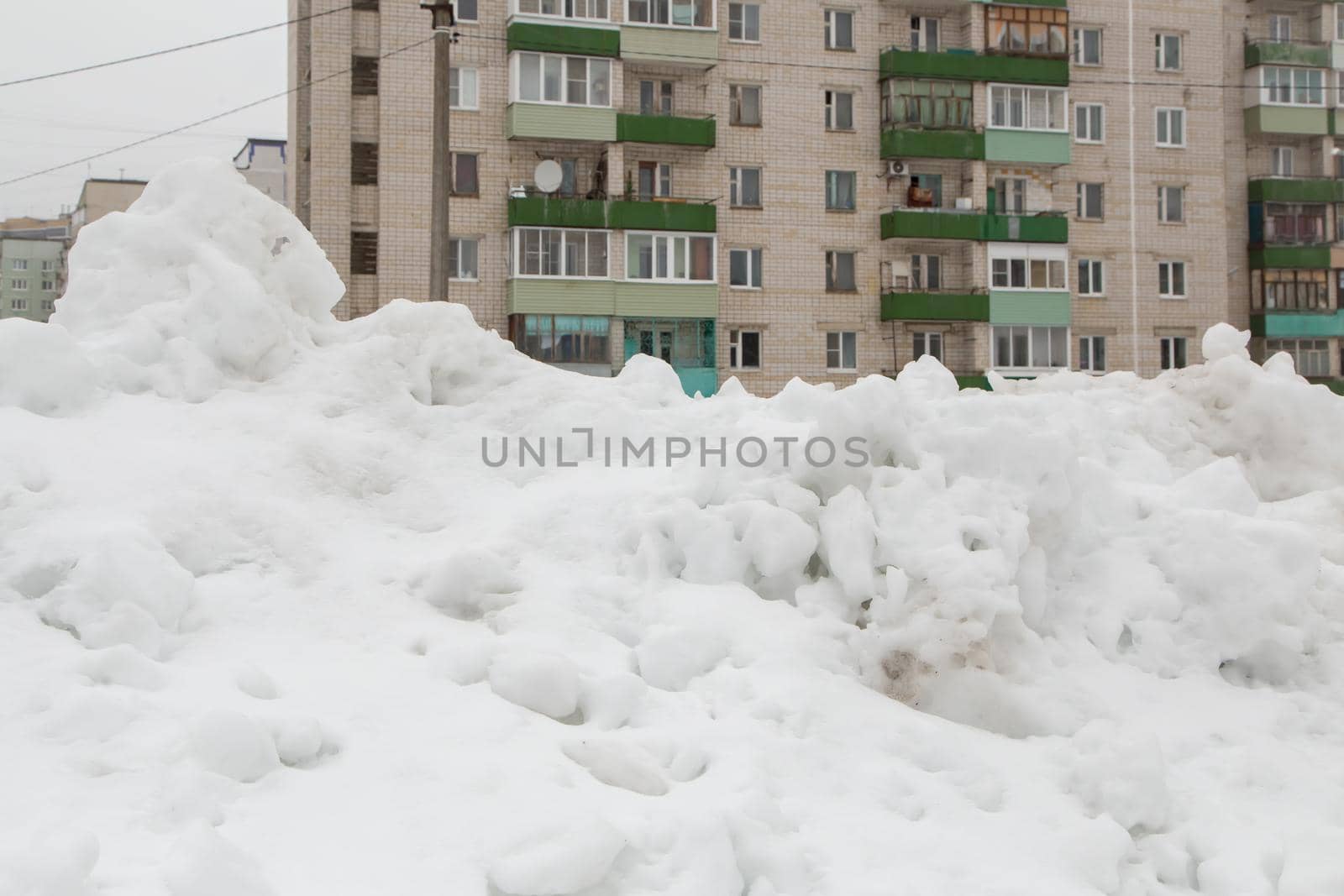 A large snowdrift in the city against the background of a multi-storey building. A block of snow with dirty lumps lies on a city street in the courtyard of a residential building.