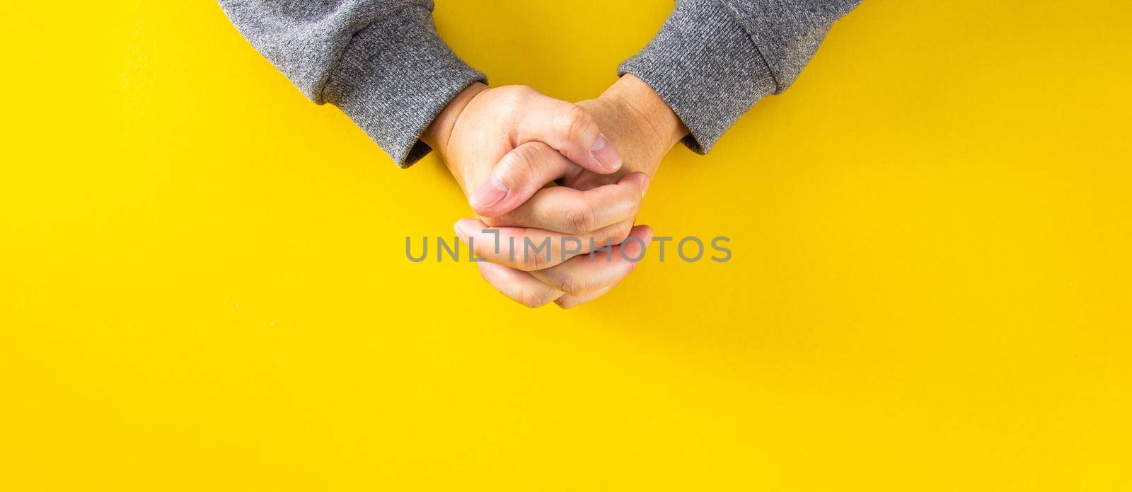 The hands of the man who was clinging to the prayer on the yellow background.Top view
