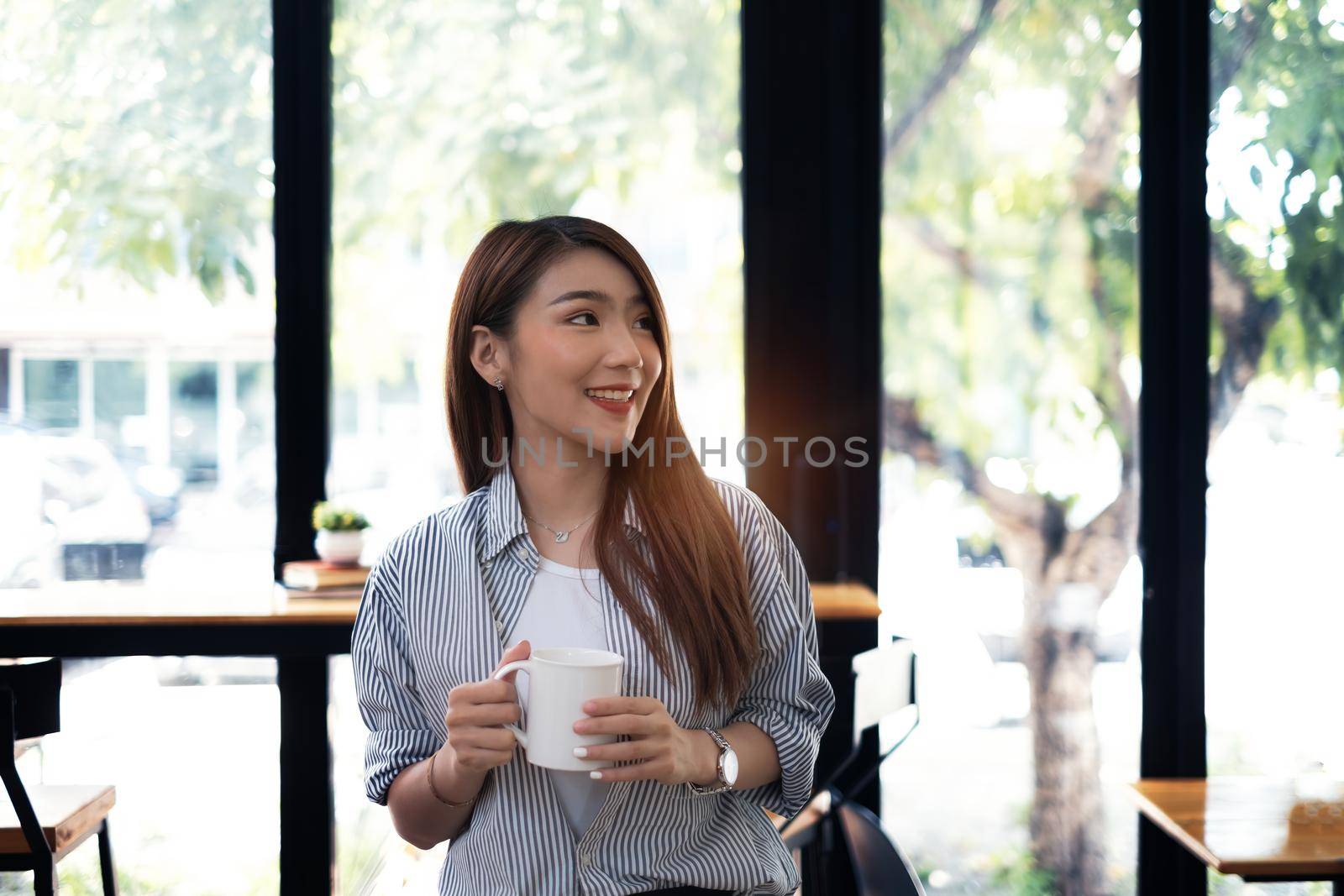 Young beautiful woman holding coffee cup and feeling fresh while sitting at her working place at monday morning