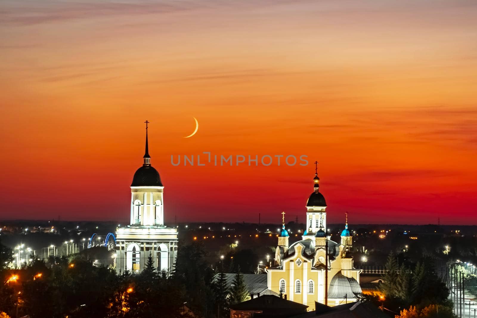 A church,temple or cathedral against the background of an evening sunset with a maroon sky and a big month.The horizon line at dawn with the moon the red sky.City panorama with sky line in the night by YevgeniySam