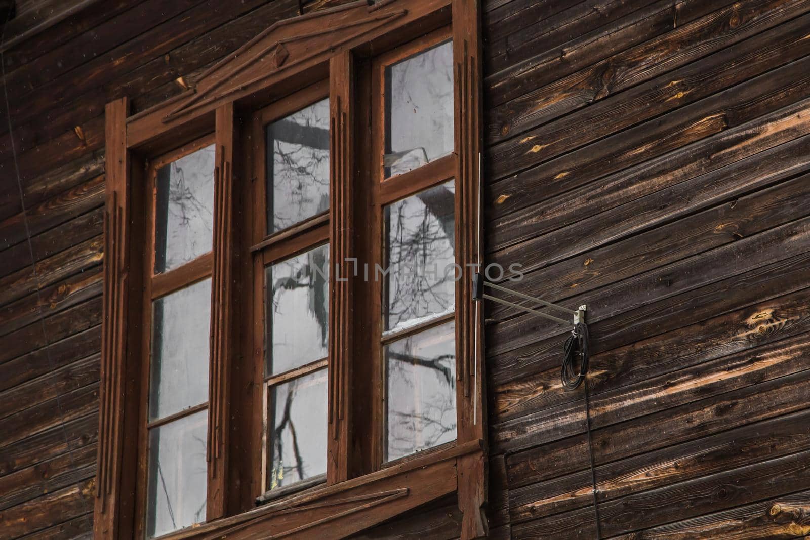 A wooden window in an old planked building with an antenna on the wall. An old wooden building in the city or countryside. Facade of a dilapidated house. Daylight.