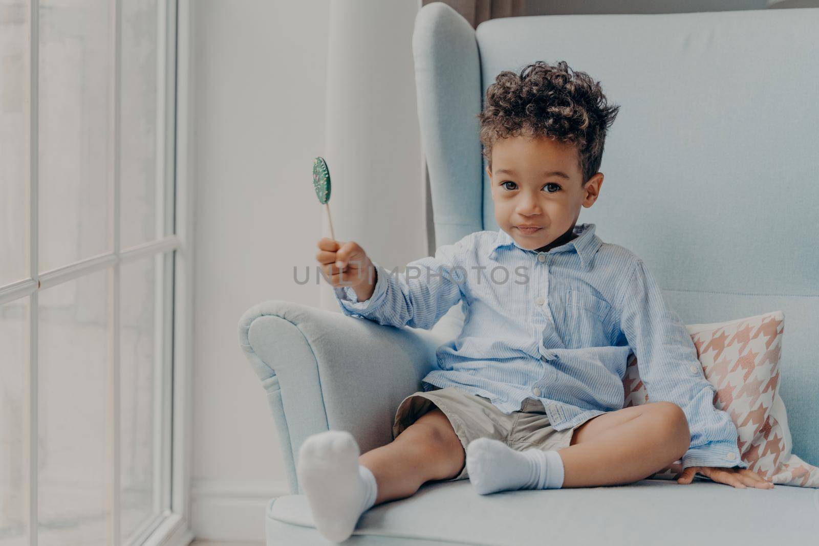 Cute little african american boy with lollipop indoors by vkstock