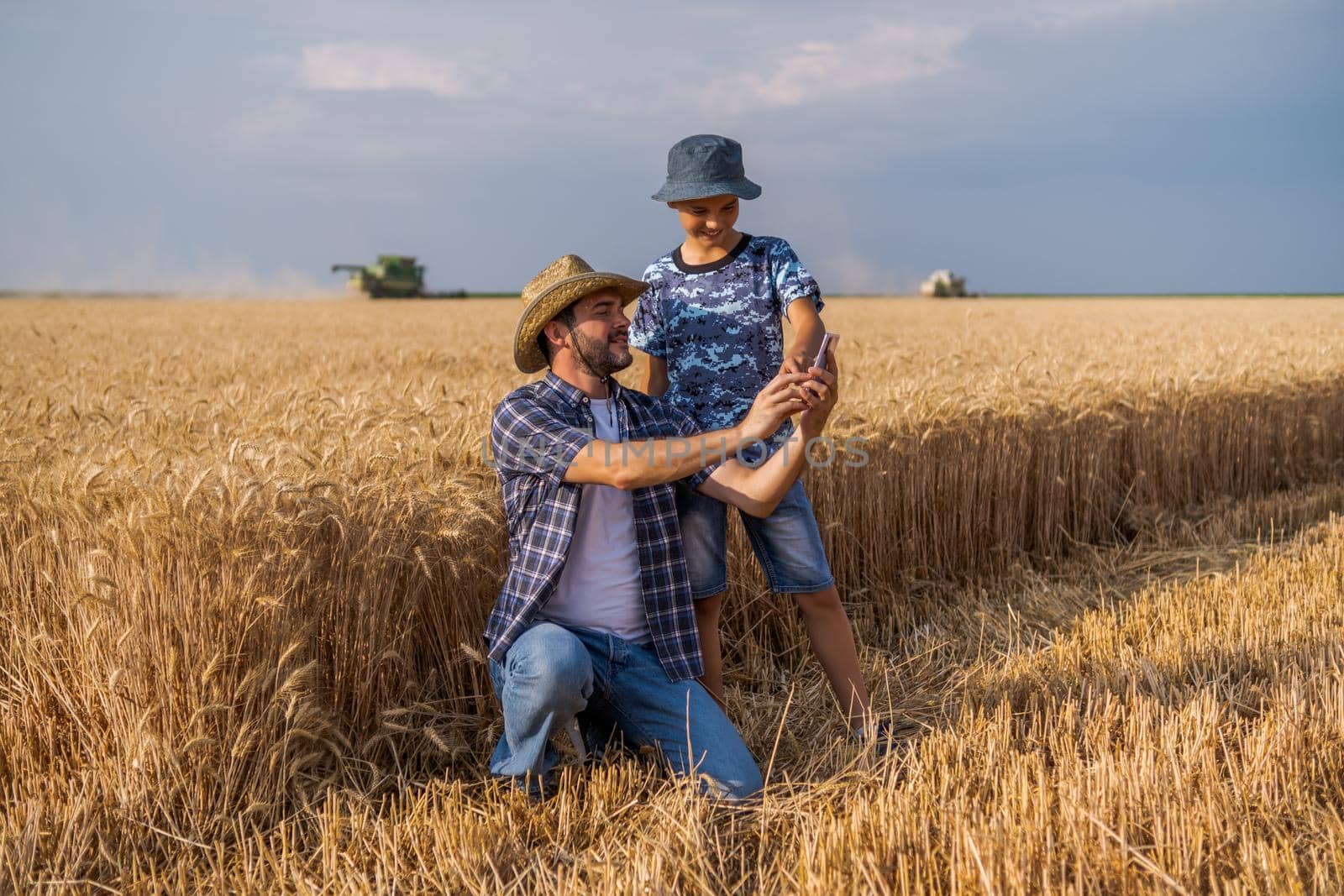 Farmers are standing in their wheat field while the harvesting is taking place. Father is teaching his son about agriculture.