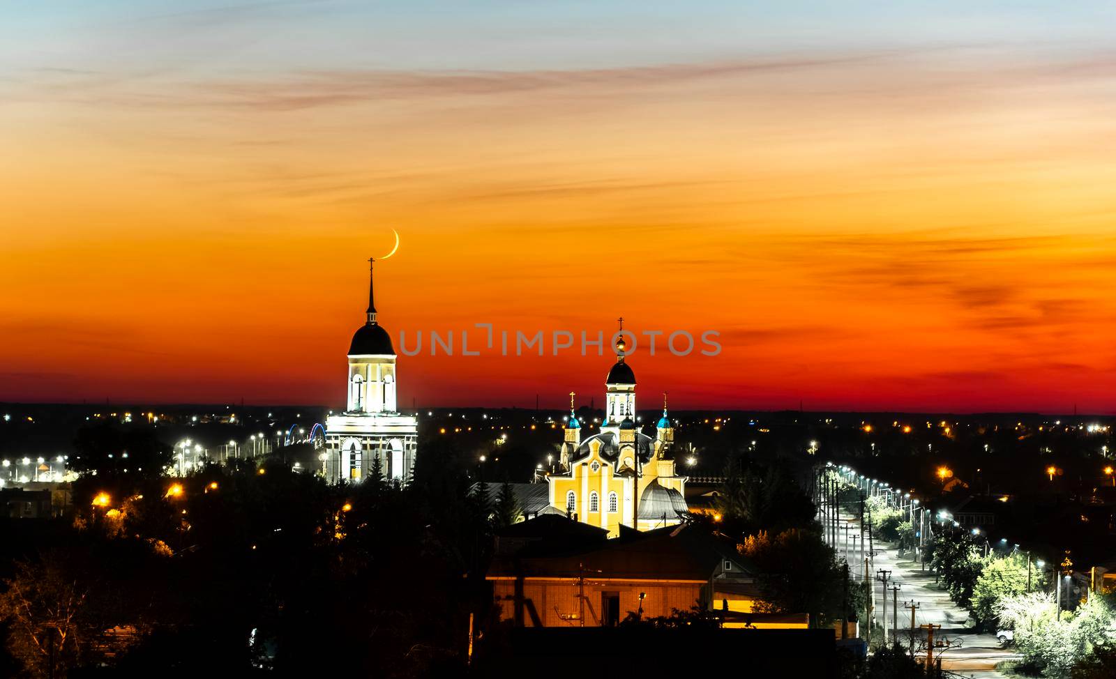 A church,temple or cathedral against the background of an evening sunset with a maroon sky and a big month.The horizon line at dawn with the moon and the red sky.City panorama with towers and domes by YevgeniySam