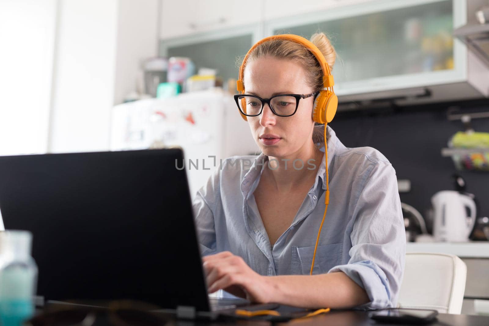 Female freelancer in her casual home clothing working remotly from her dining table in the morning. Home kitchen in the background. Stay healthy and stay at home during corona virus pandemic.