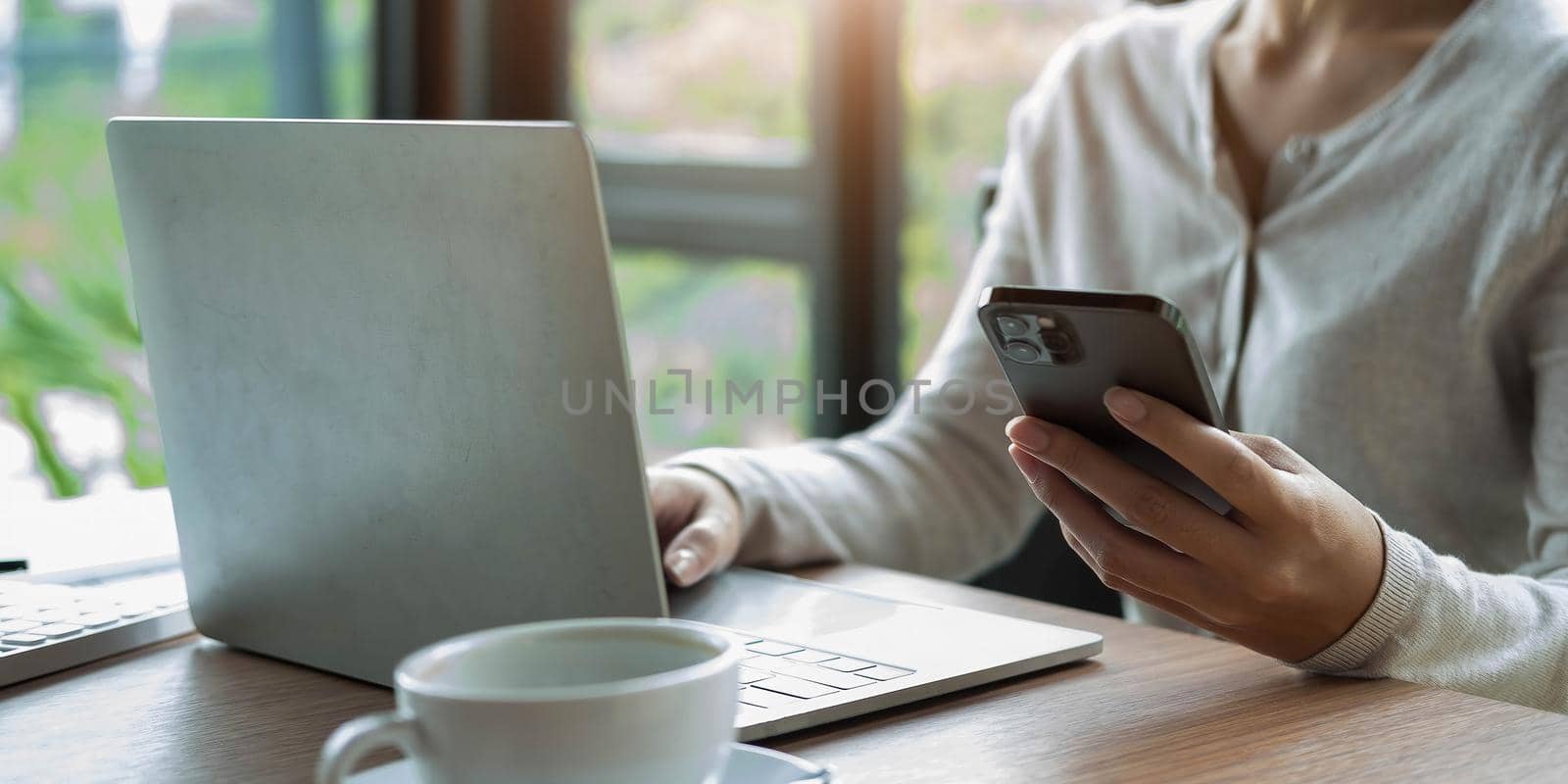 Woman's hands using laptop and mobile phone at the office by wichayada