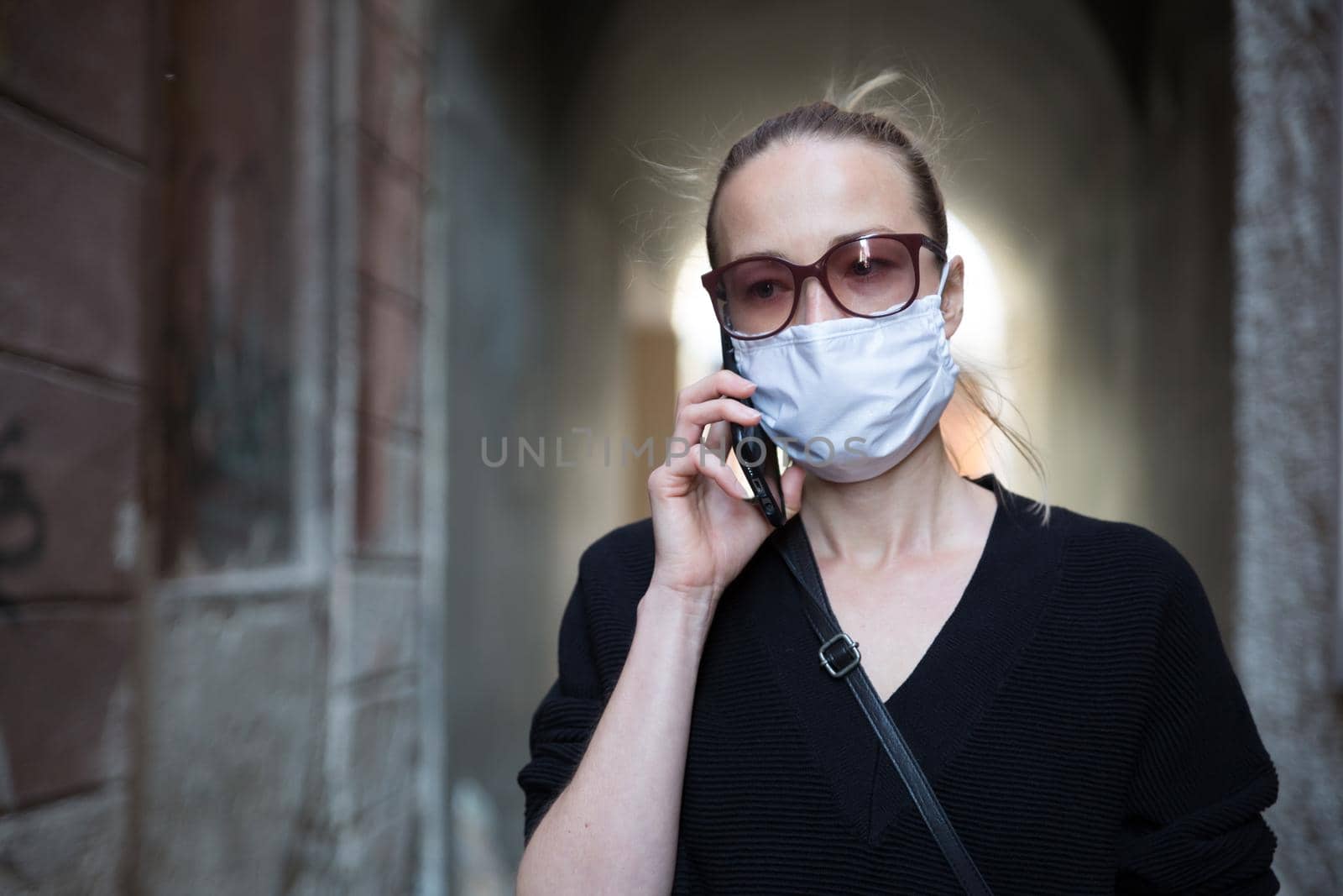 COVID-19 pandemic coronavirus. Casual caucasian woman at medieval city street using mobile phone, wearing protective face mask against spreading of coronavirus and disease transmission by kasto