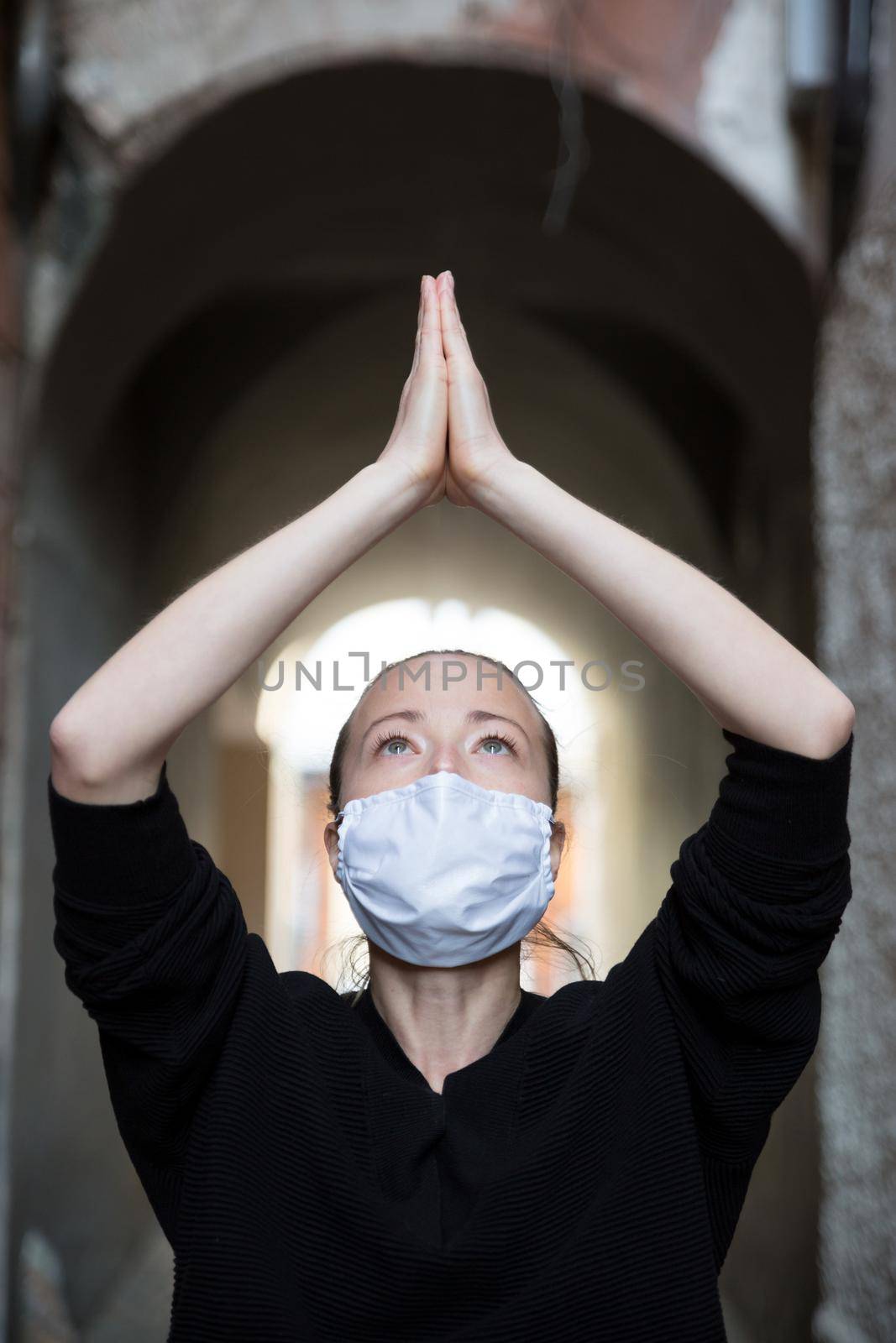 Coronavirus outbreak. Young caucasian woman wearing medical protection face mask praying over coronavirus global pandemic, for salvation of humanity, health, anxiety and depression reduction...
