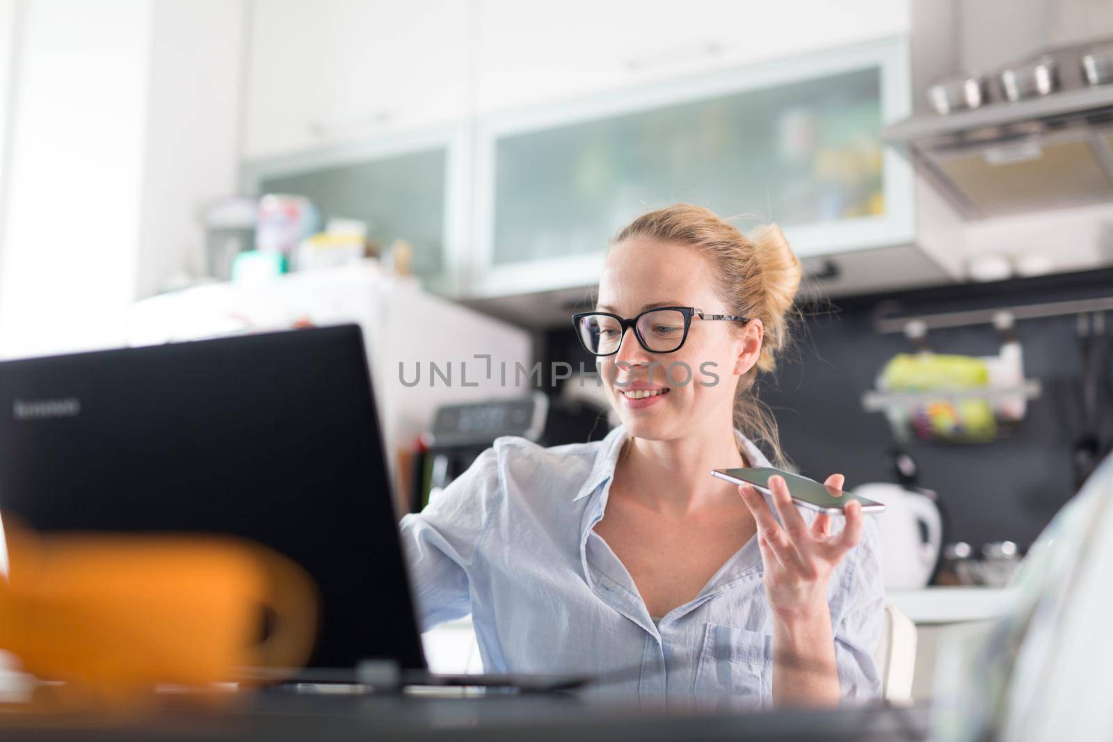 Stay at home and social distancing. Woman in her casual home clothing working remotly from kitchen dining table. Video chatting using social media with friend, family, business clients or partners.