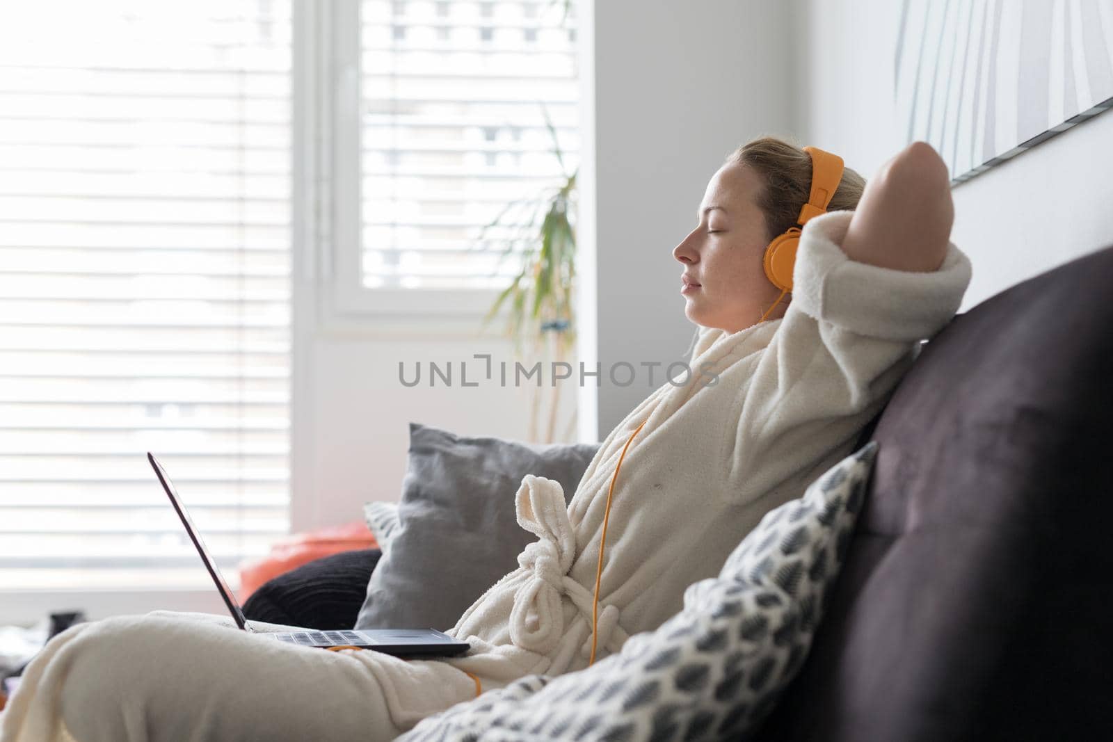 Stay at home, shelter in place and social distancing. Woman in her casual home bathrobe stretching and relaxing while working remotly from her living room. Using social media apps for video chatting by kasto