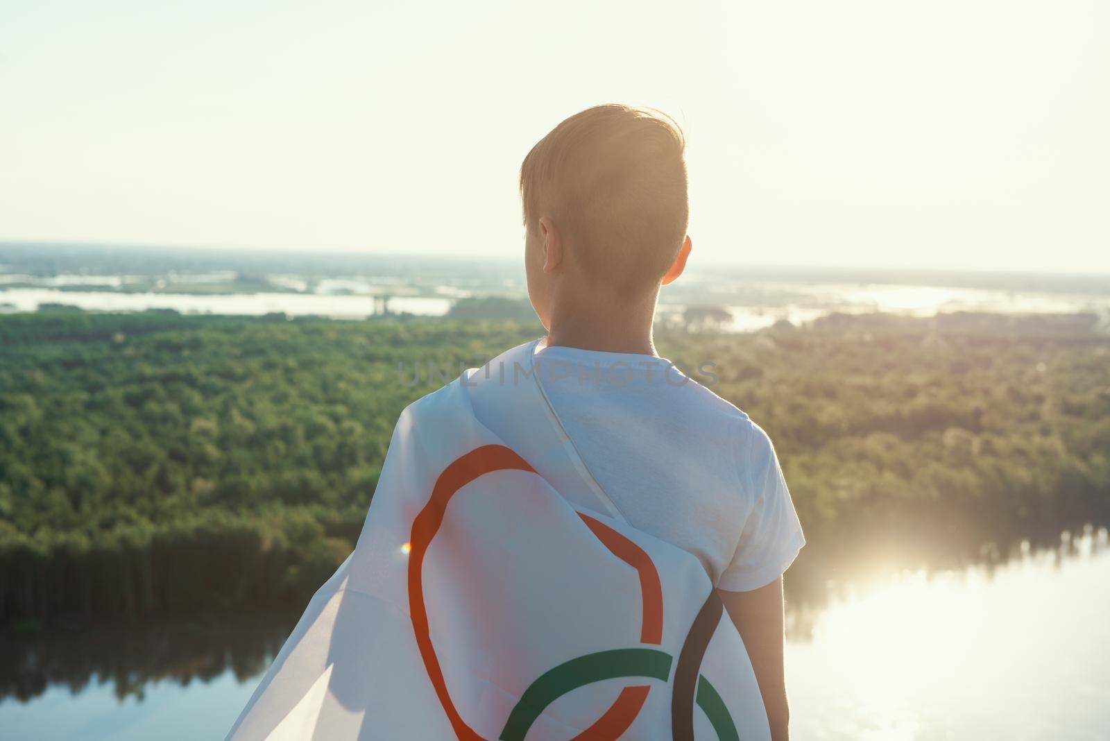 Blonde boy waving waving flag the Olympic Games outdoors over blue sky at the river bank by rusak