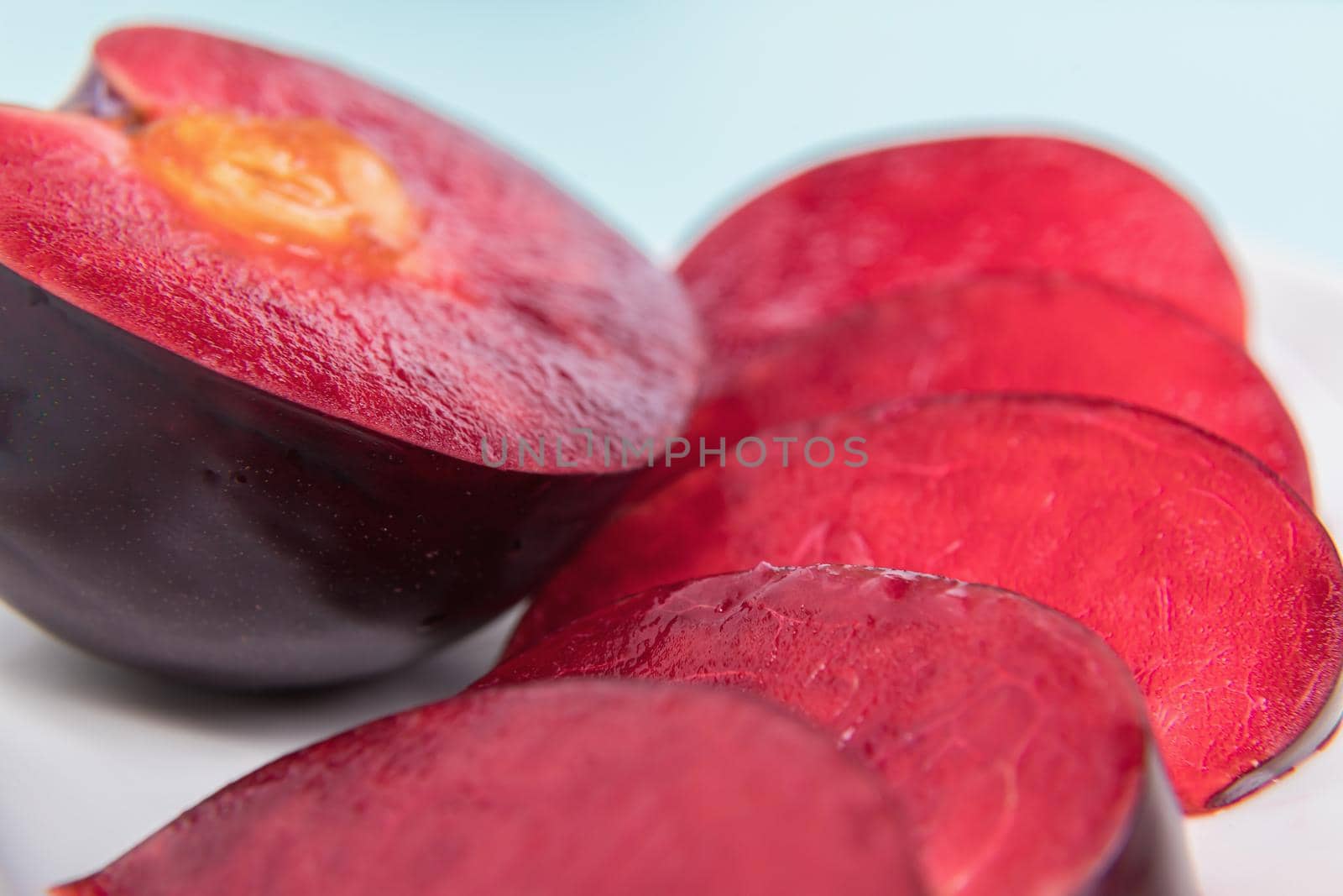 On a white saucer, a large plum, cut in half, with slices next to it. The pulp of red berries. Close-up.